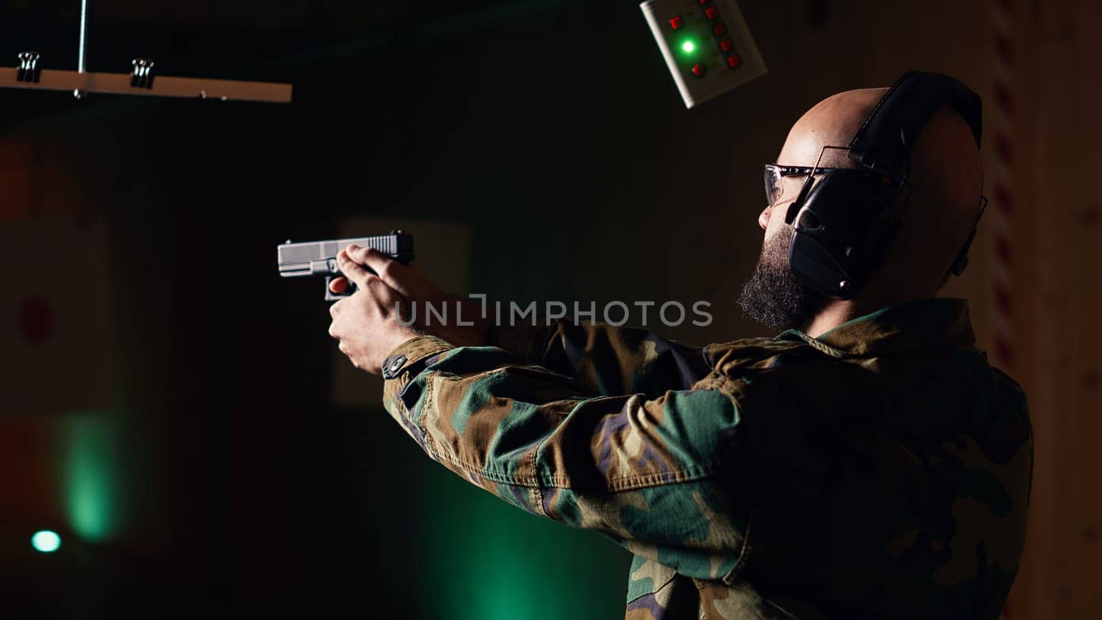 Portrait of happy man training in shooting range, learning pistol holding etiquette, engaging targets at extended range. Joyous army soldier firing lethal fire weapon, camera B