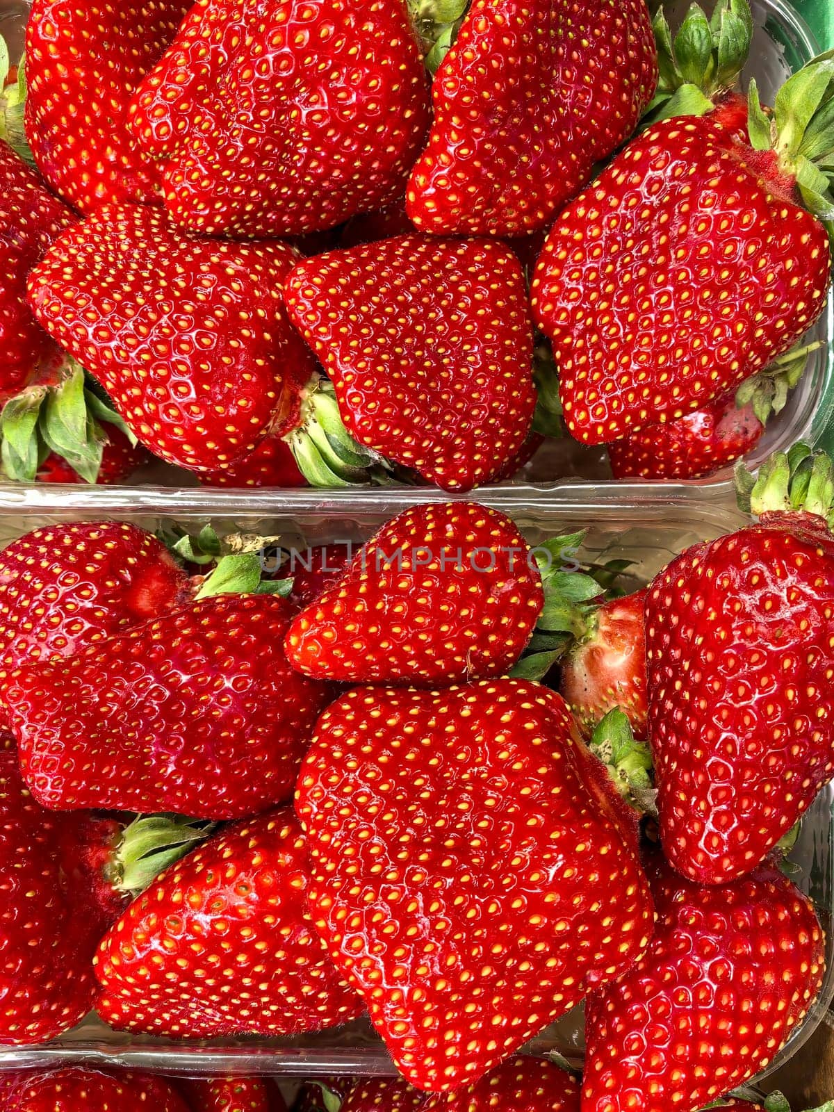 Fresh ripe strawberries fill plastic containers, showcasing their vibrant red color and texture. Ideal for promoting healthy eating. Made on smartphone.
