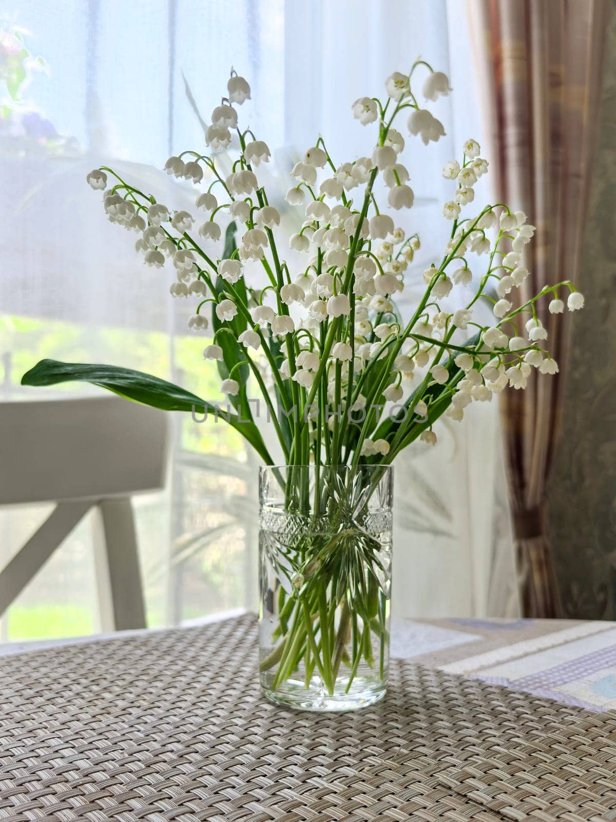 Lily of the valley flowers elegantly arranged in a clear glass vase on a table. The delicate blooms create a serene and natural atmosphere in a room. Made on smartphone.