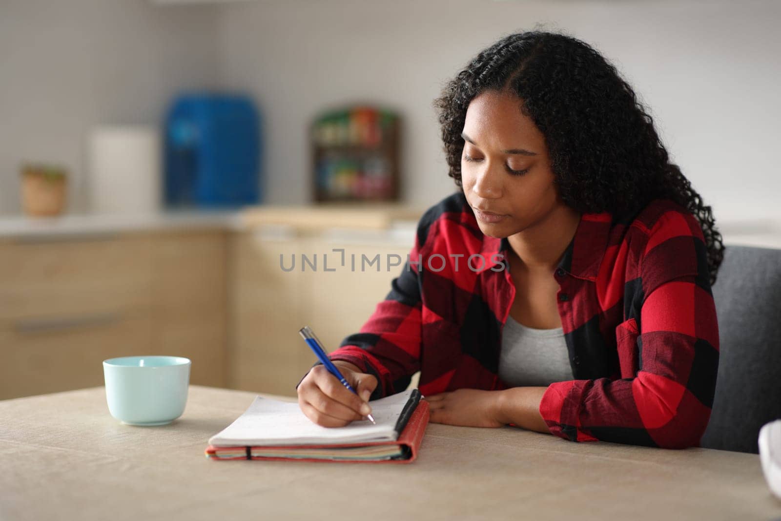 Concentrated black student learning writing notes in the kitchen at home