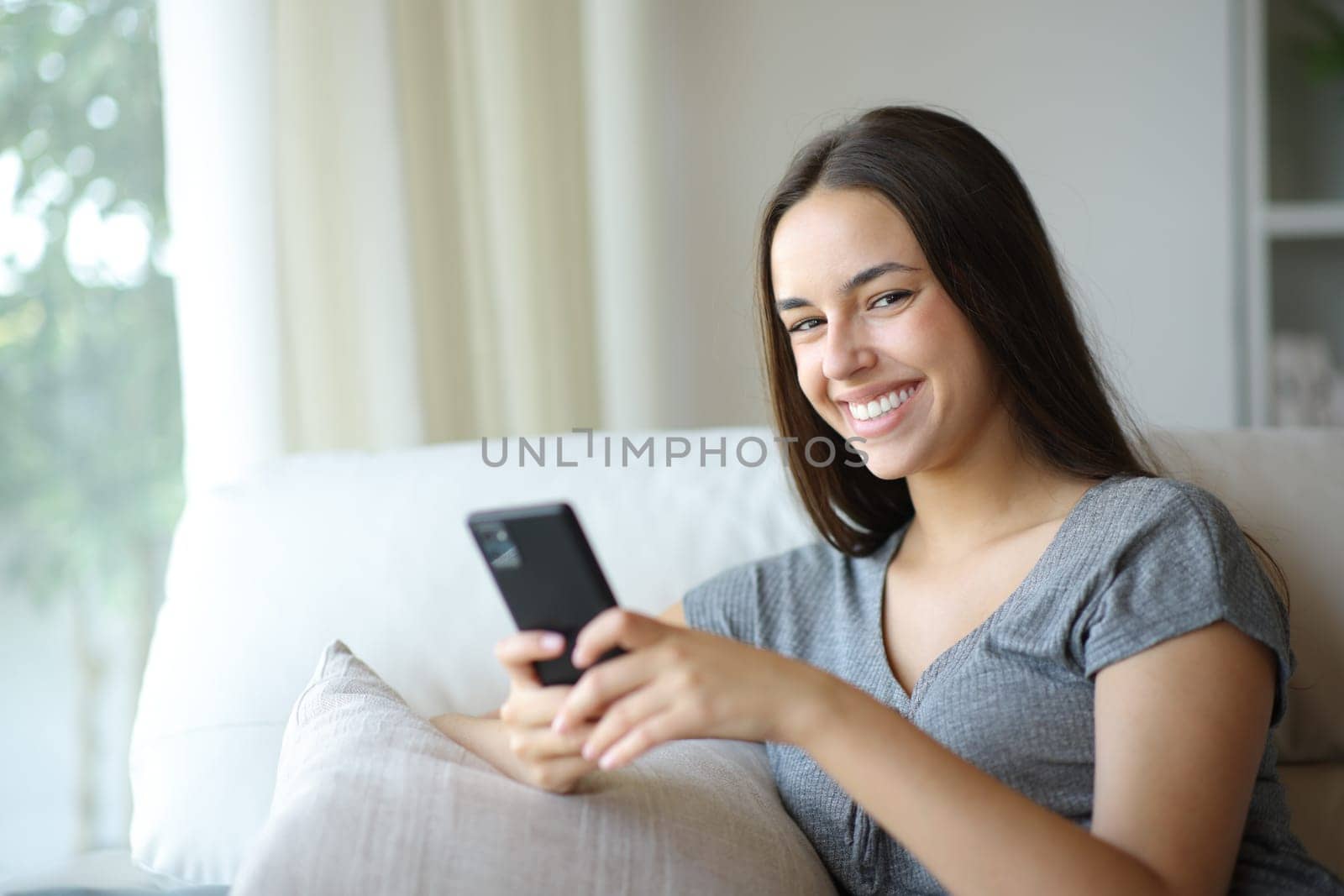 Happy woman posing holding mobile phone sitting in a couch at home