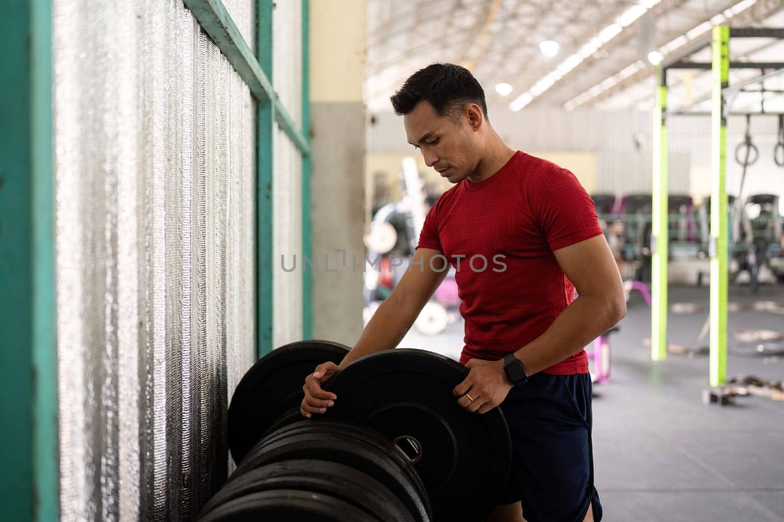 A focused male athlete adjusts weights at a gym, embodying dedication to fitness and strength training.