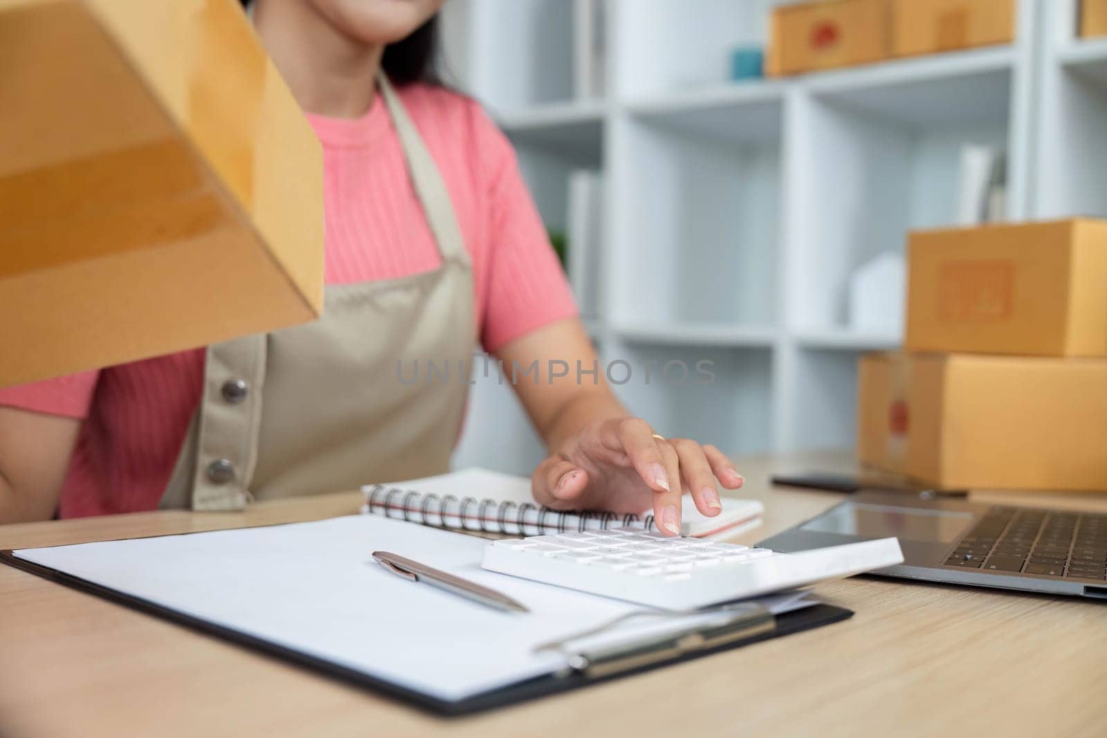 A dedicated entrepreneur manages her small business by organizing packages and maintaining a detailed notebook in her workspace.