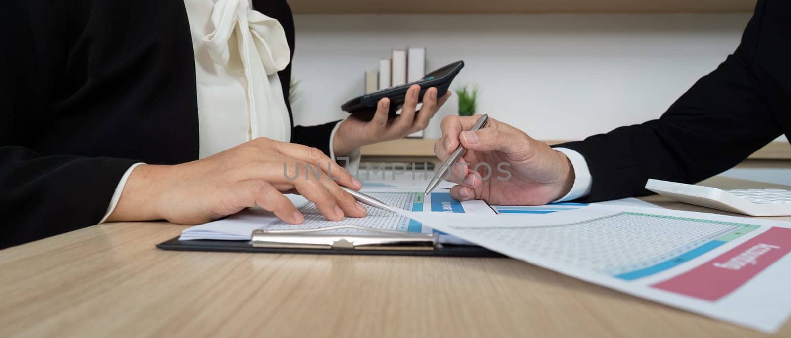 Two business professionals collaborating over financial reports and calculations, showcasing teamwork in a corporate setting.