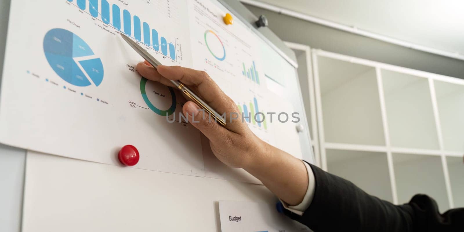 A business professional pointing at budget graphs on a whiteboard, highlighting financial insights and data visualization.