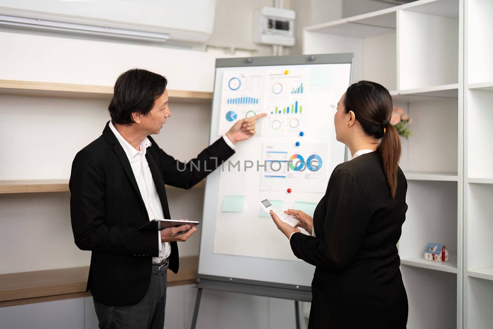 A male consultant discusses financial charts while a female colleague takes notes in a modern office.