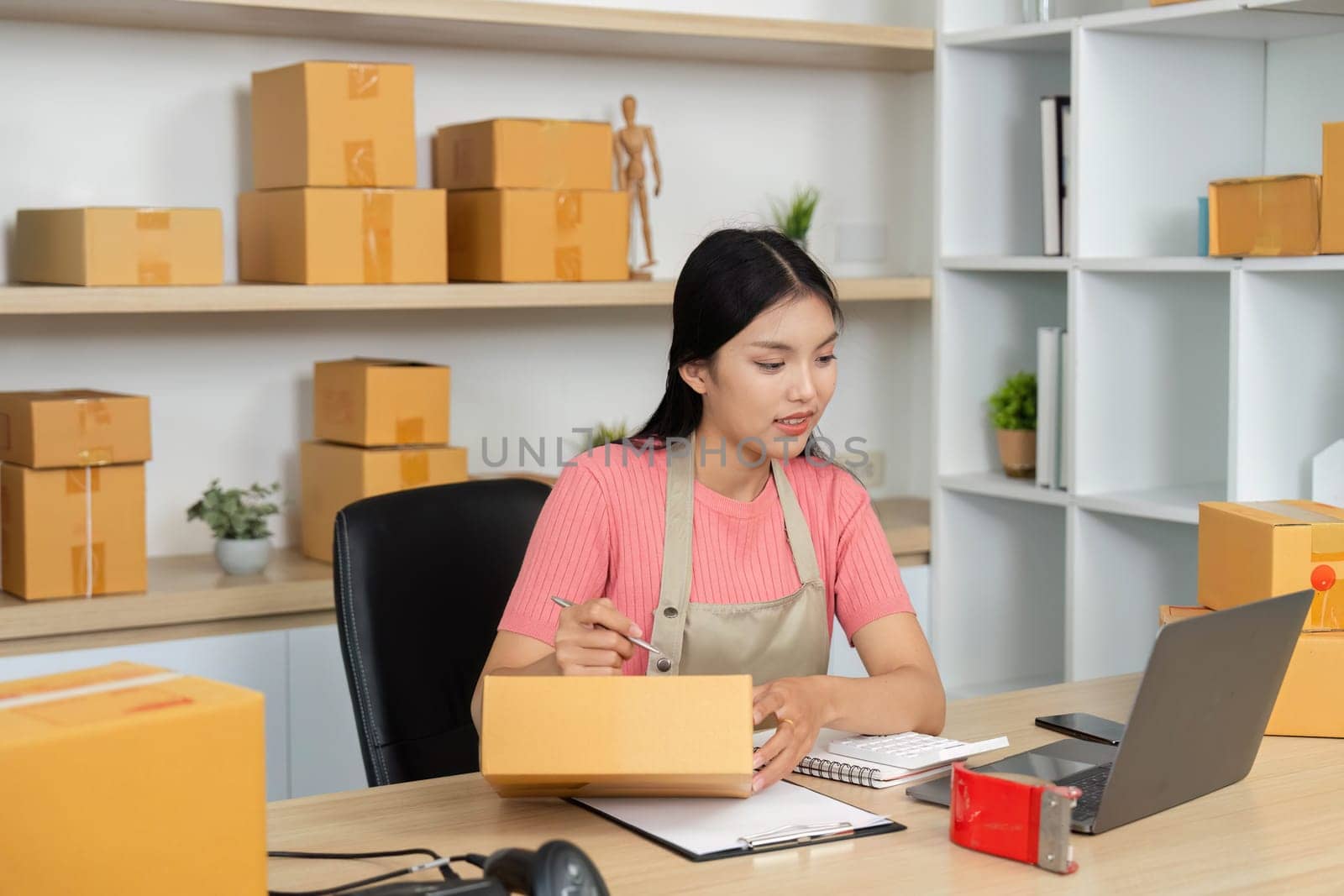 A focused entrepreneur organizes packages and notes in her small business workspace, showcasing efficiency and dedication.