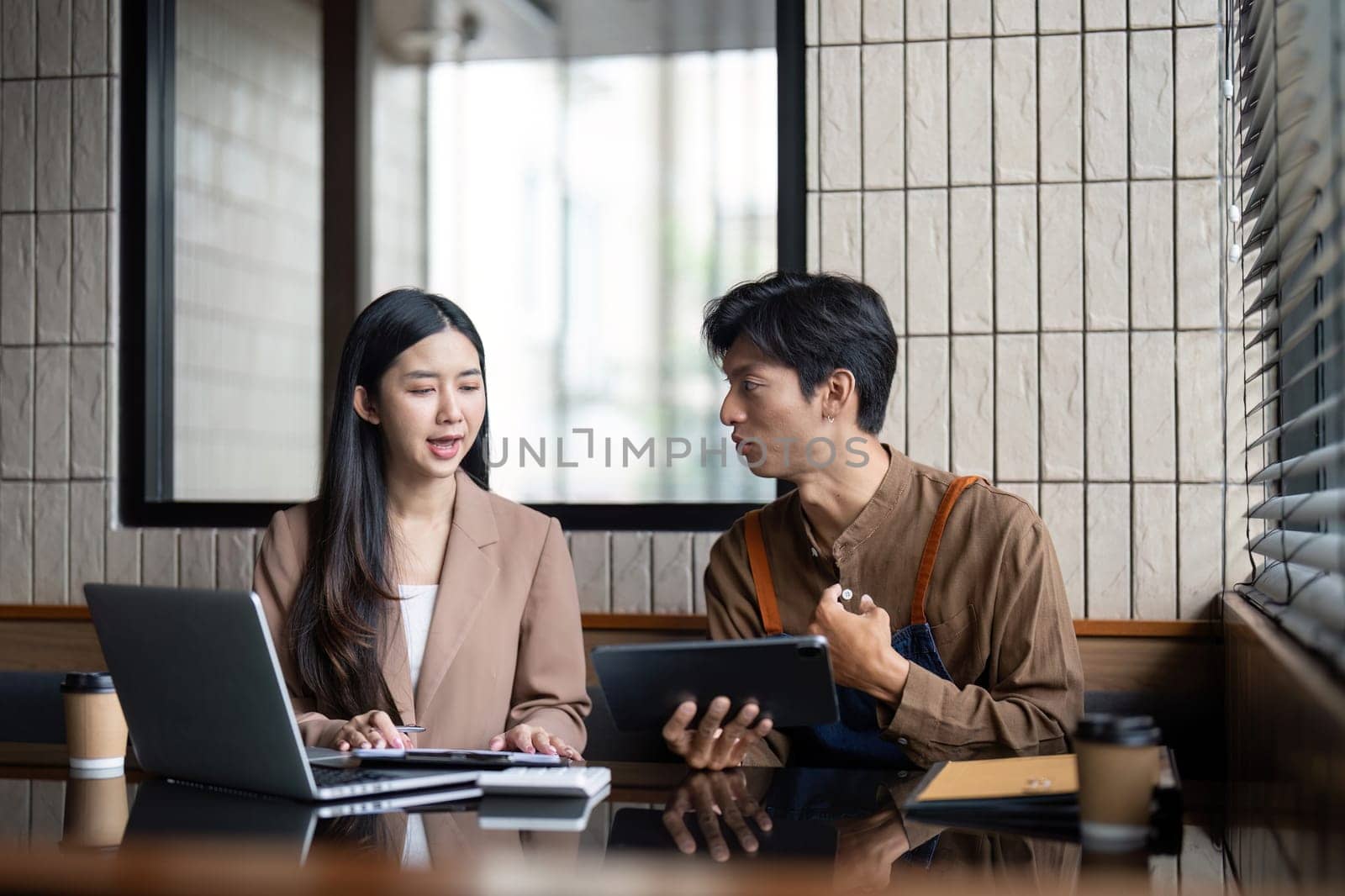 A man and woman engaged in a focused conversation, reviewing documents and digital content in a contemporary workspace.