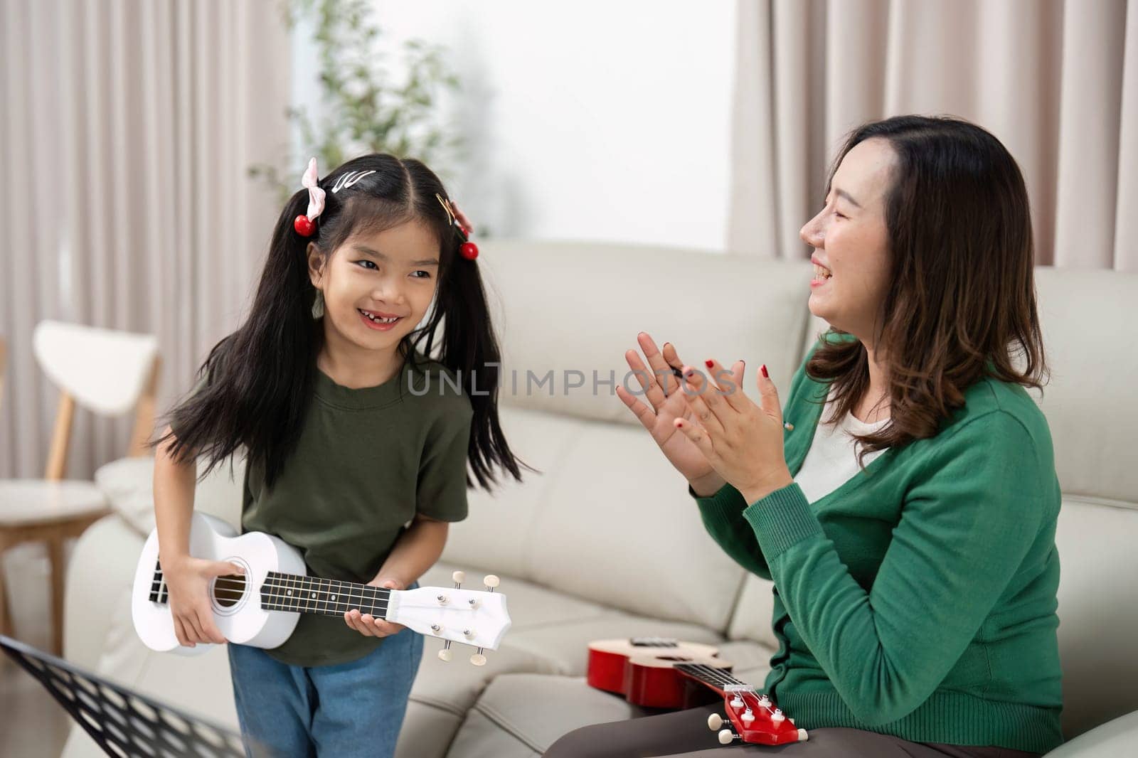 A mother and daughter share a delightful moment as the girl plays the ukulele, showcasing the joy of music and family bonding.