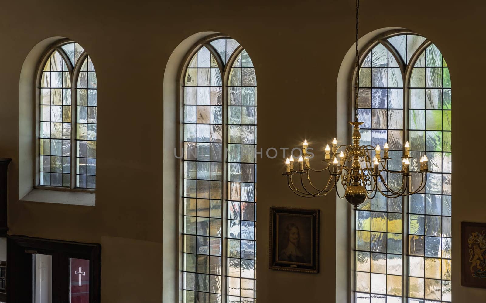 Royal Tunbridge Wells, UK - Apr 29, 2025 - A stunning view of Chandelier hanging from the ceiling and Large stained glass windows in the background inside of The Church of King Charles the Martyr. use it as your Wallpaper, Poster and Space for text, Selective focus.