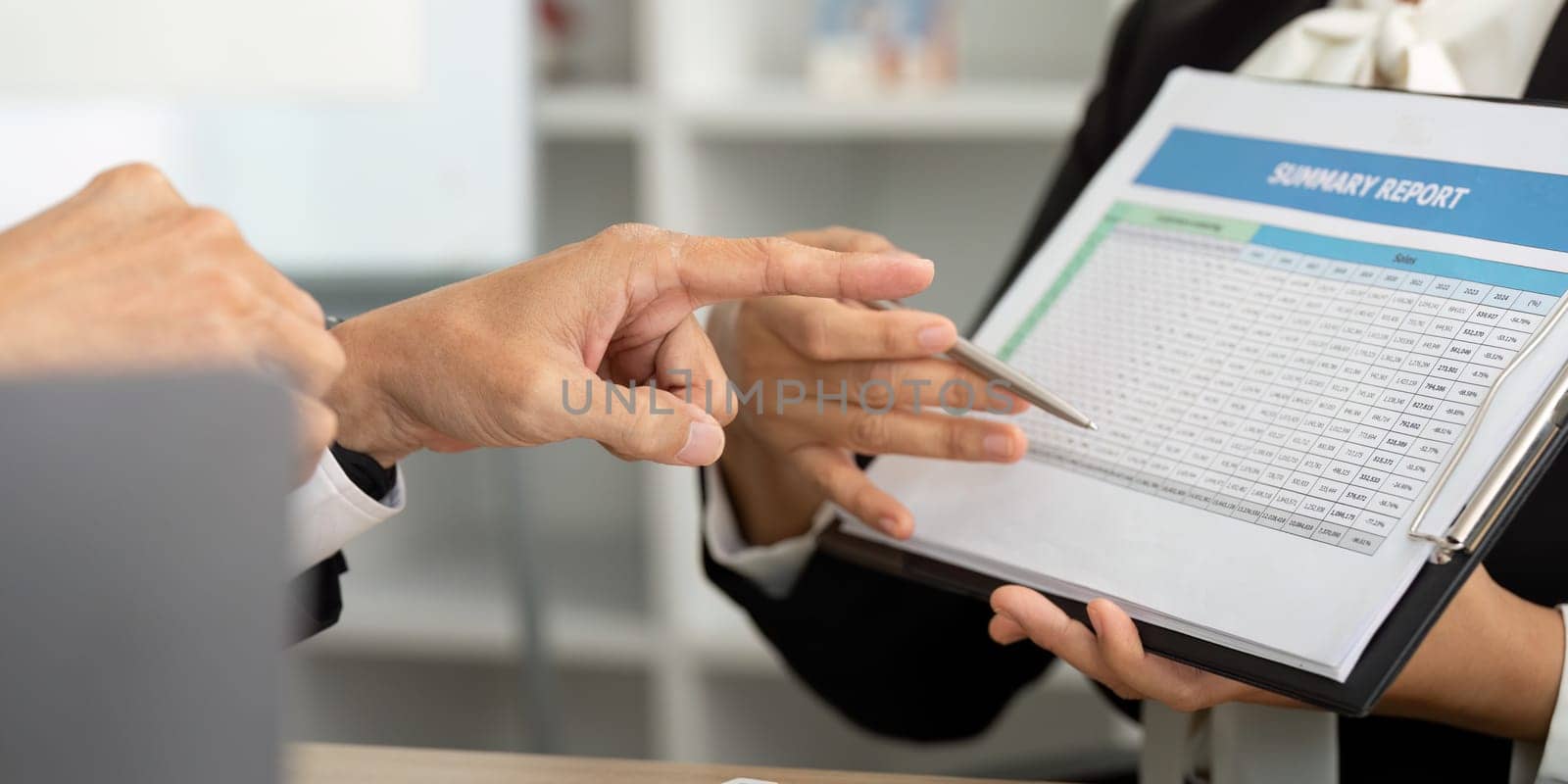 Two business professionals discussing a summary report while analyzing data on a clipboard. Focus on teamwork and financial planning.