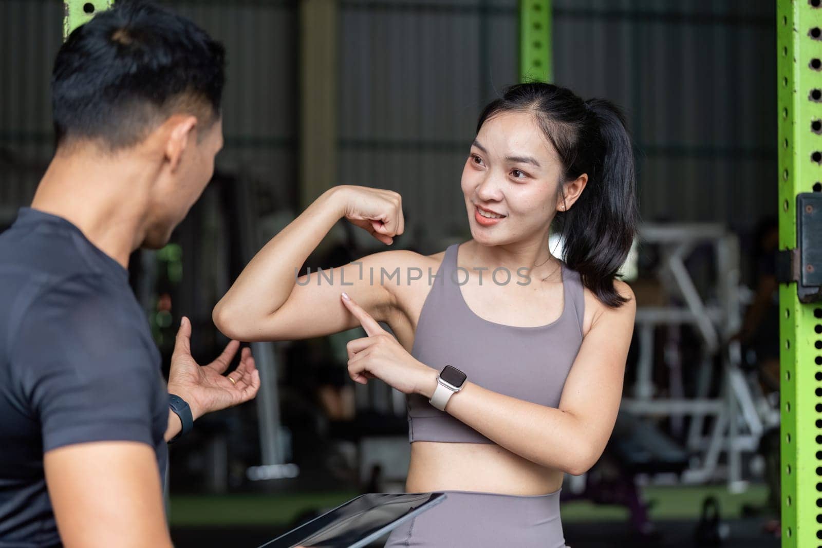 A fitness coach and a young woman engage in a personal training session, focusing on strength and wellness in a gym environment.