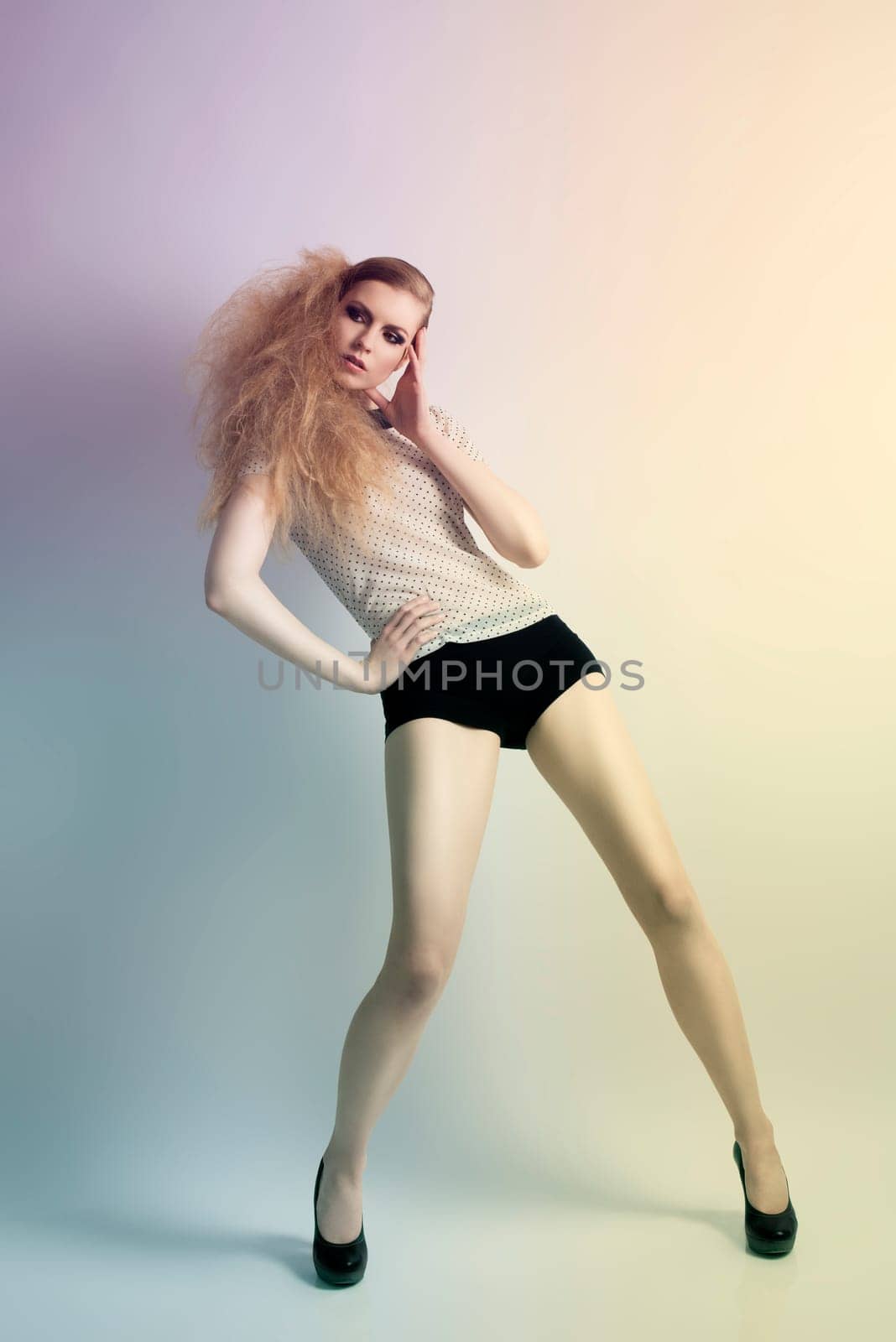 Cute blonde woman with creative hair-style in fashion pose wearing shirt with pois pattern, black shorts and heels