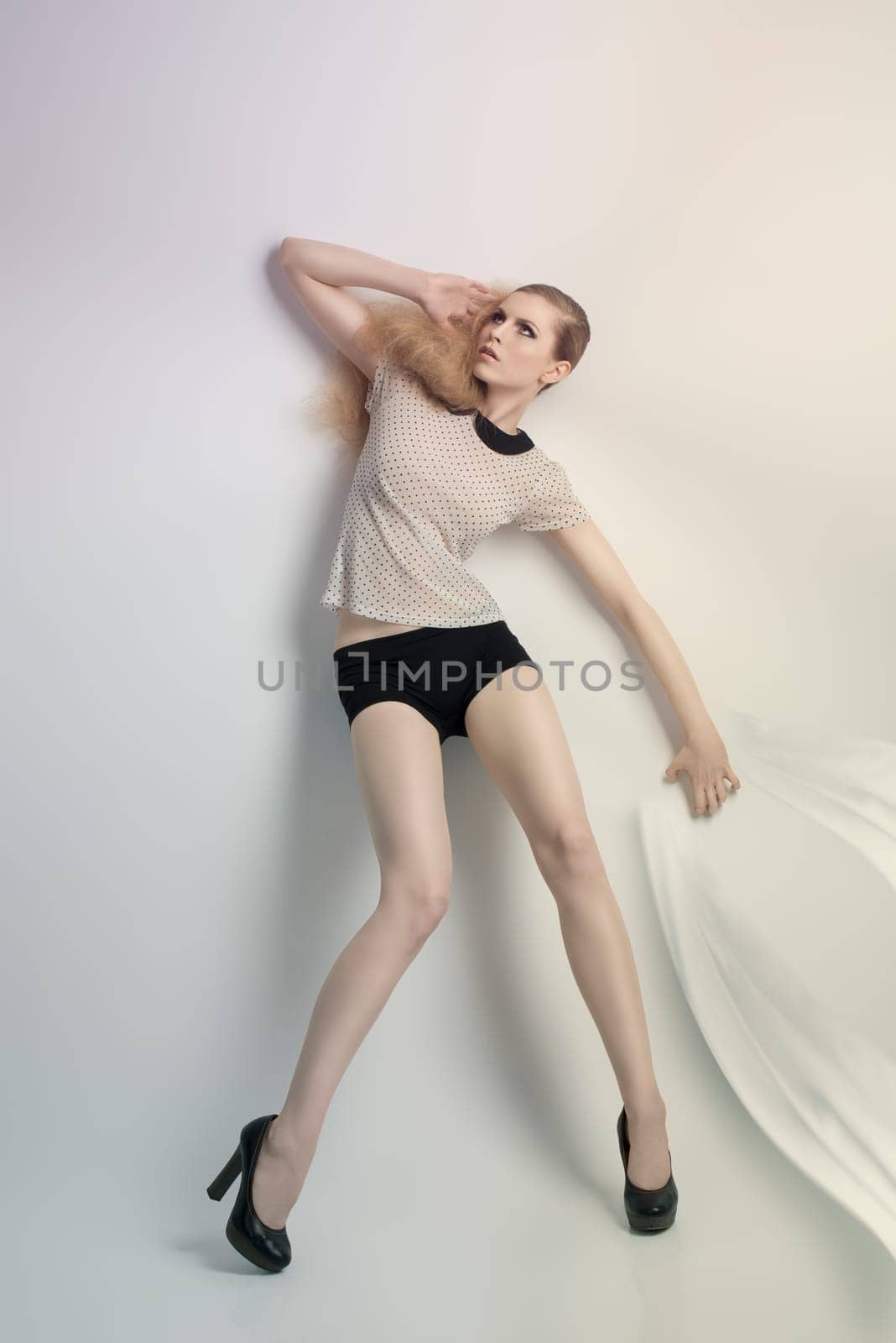 sensual blonde woman posing in fashion portrait with creative hair-style and cute make-up. She wearing pois shirt, sexy shorts and black heels