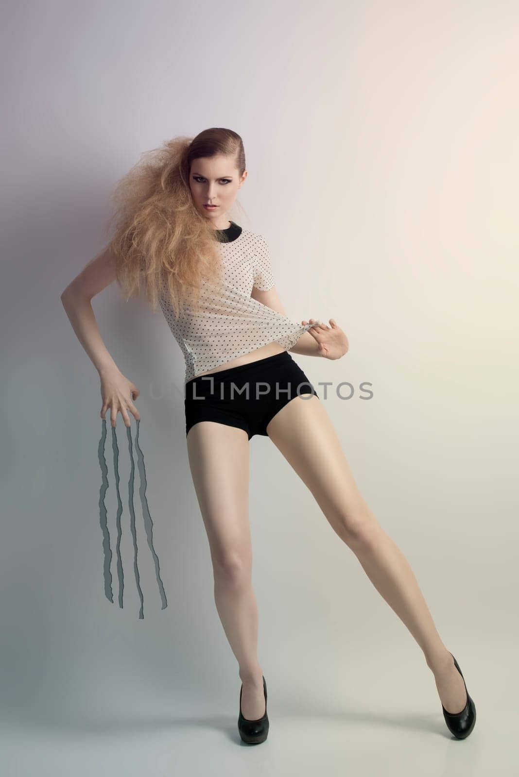sexy  blonde woman in fashion full-length portrait with creative hair-style and cute make-up. She wearing pois shirt, sexy shorts and black heels