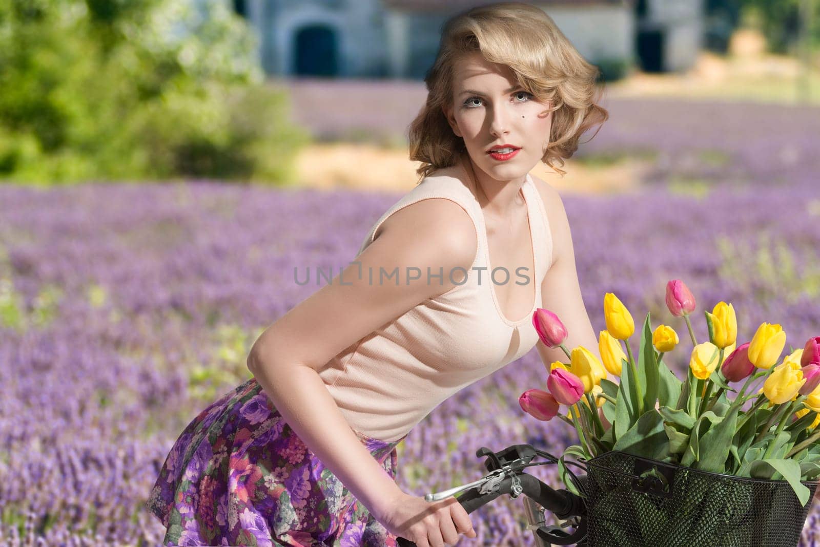 sexy  blonde girl on the bicycle with colourful tulips in the basket. She wearing pink  tank and short floral skirt. with lavander field in background