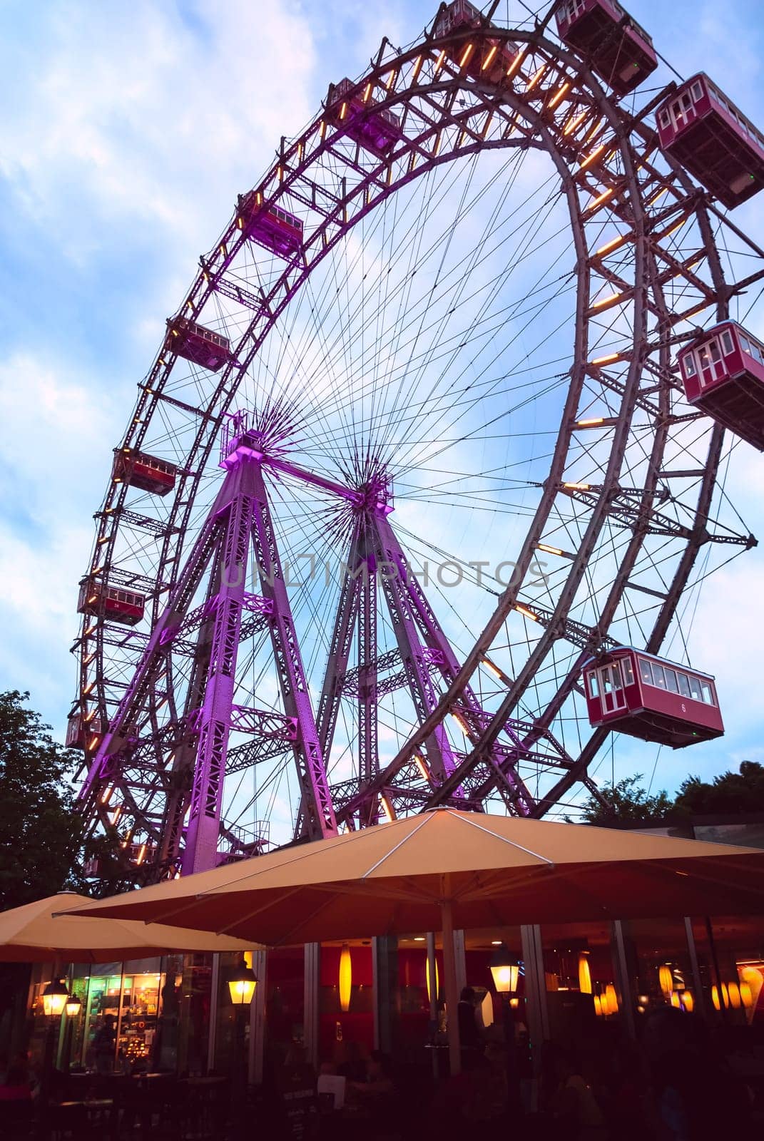 Historic Ferris wheel called Wiener Riesenrad in central public park or Prater park, Vienna, Austria, at cloudy dusk. Outdoor cafes