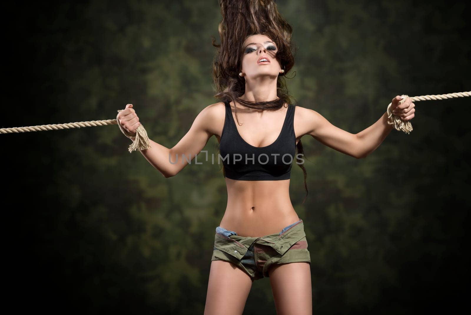 strong sensual brunette girl tied by rope with flying hair and sexy top and shorts