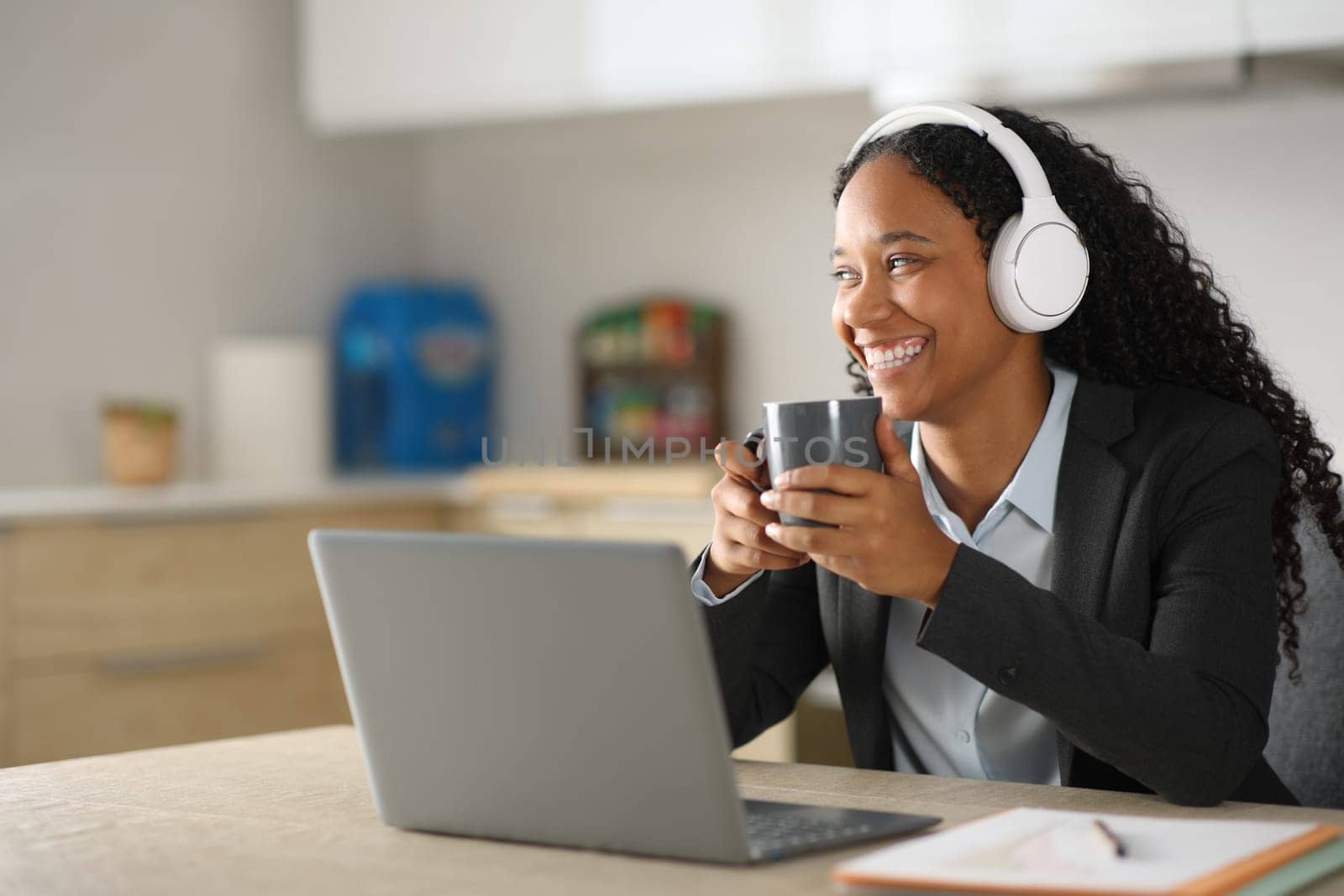 Happy black executive working online at breakfast using laptop and haedphone