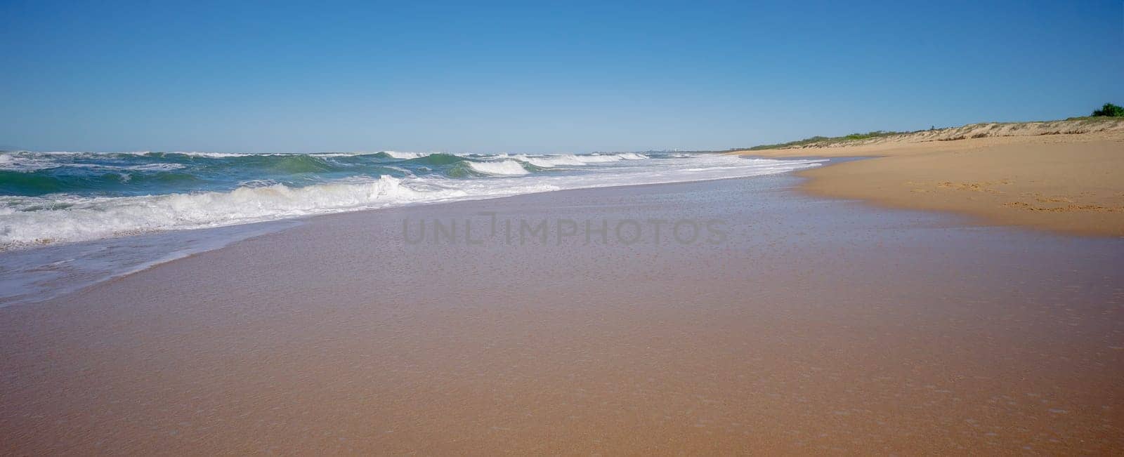 A beautiful day at Kawana Warana Beach, Sunshine Coast, Queensland. It's Autumn and the sky is blue, and the surf waves with big white foam tops break out wide, and roll towards the shore before crashing and flowing  across the sandy beach.