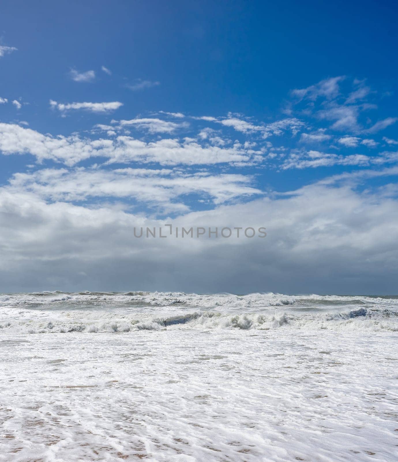 A coastal background image of very rough wild dangerous sea along the shoreline with blue sky and storm clouds on the horizon