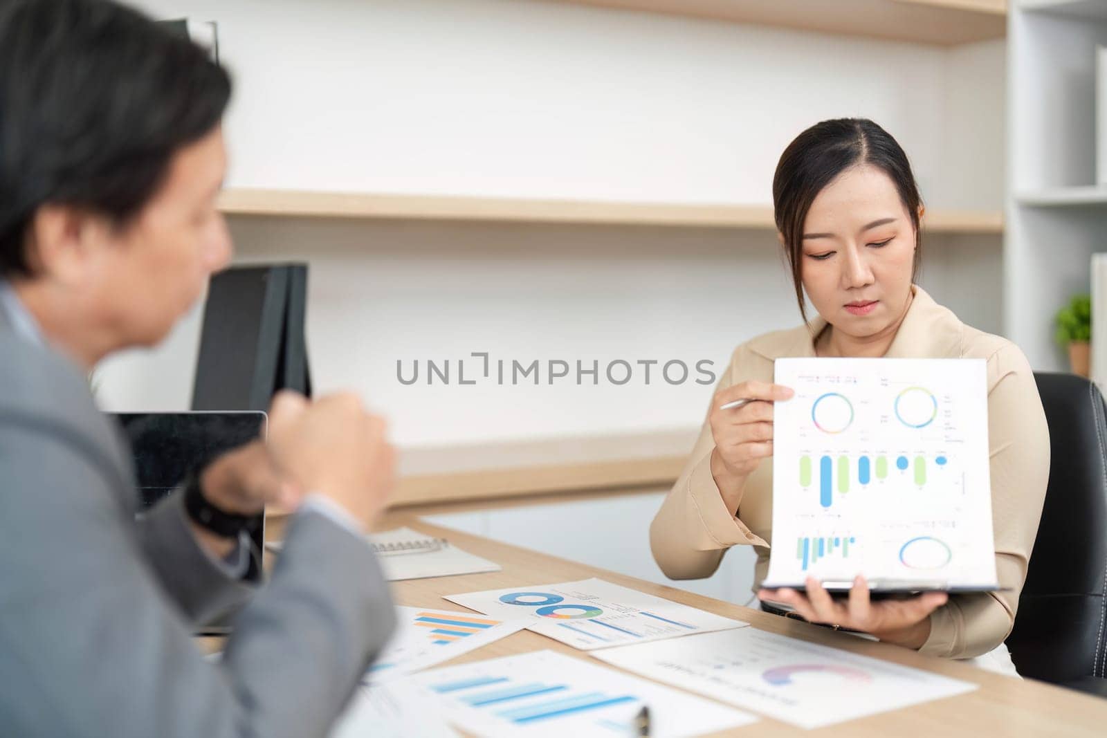 A businesswoman presents financial graphs to her colleague during a meeting, focusing on data analysis and strategy.