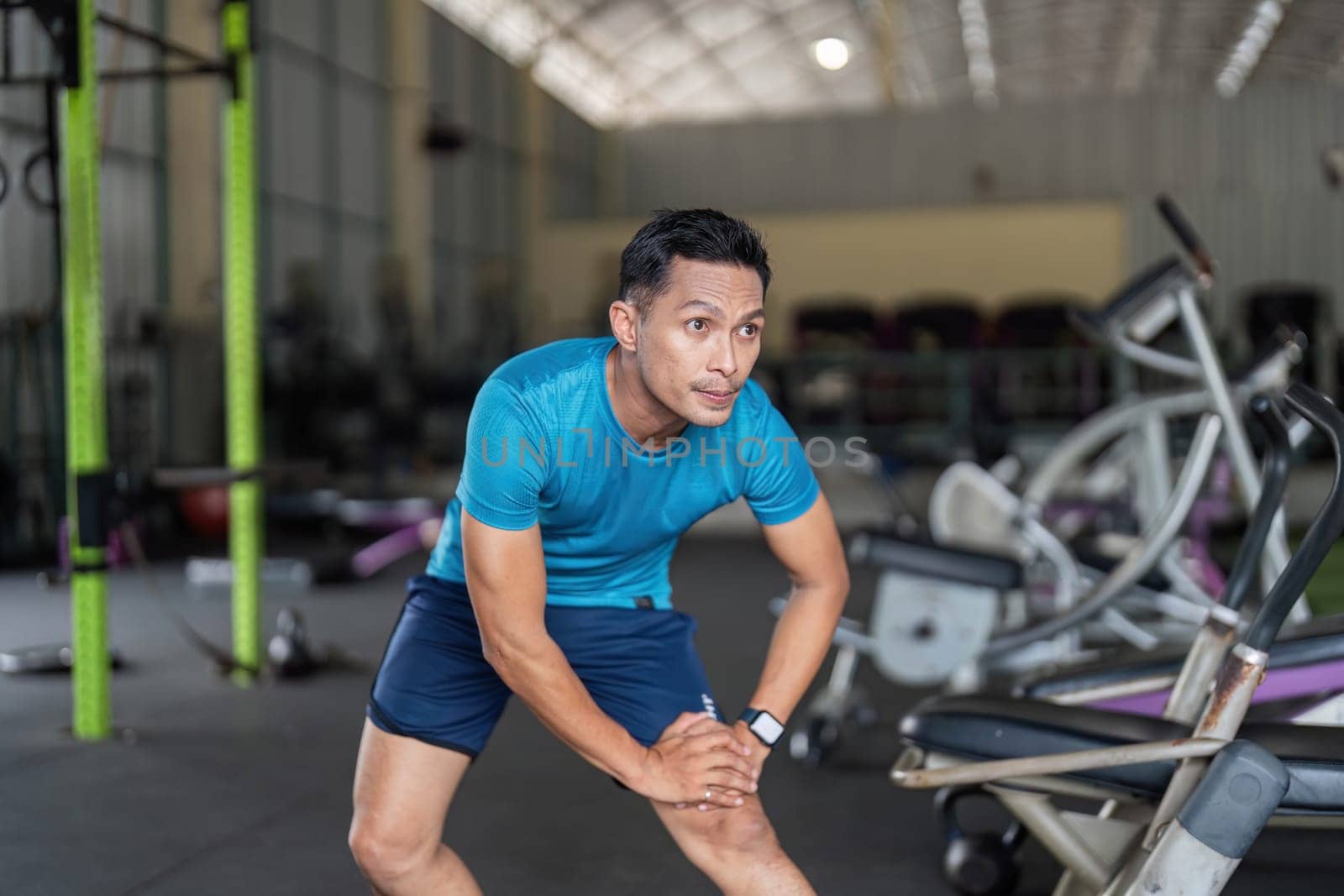 A fit man engages in a stretching routine at a gym, focusing on flexibility and warm-up exercises to enhance performance.