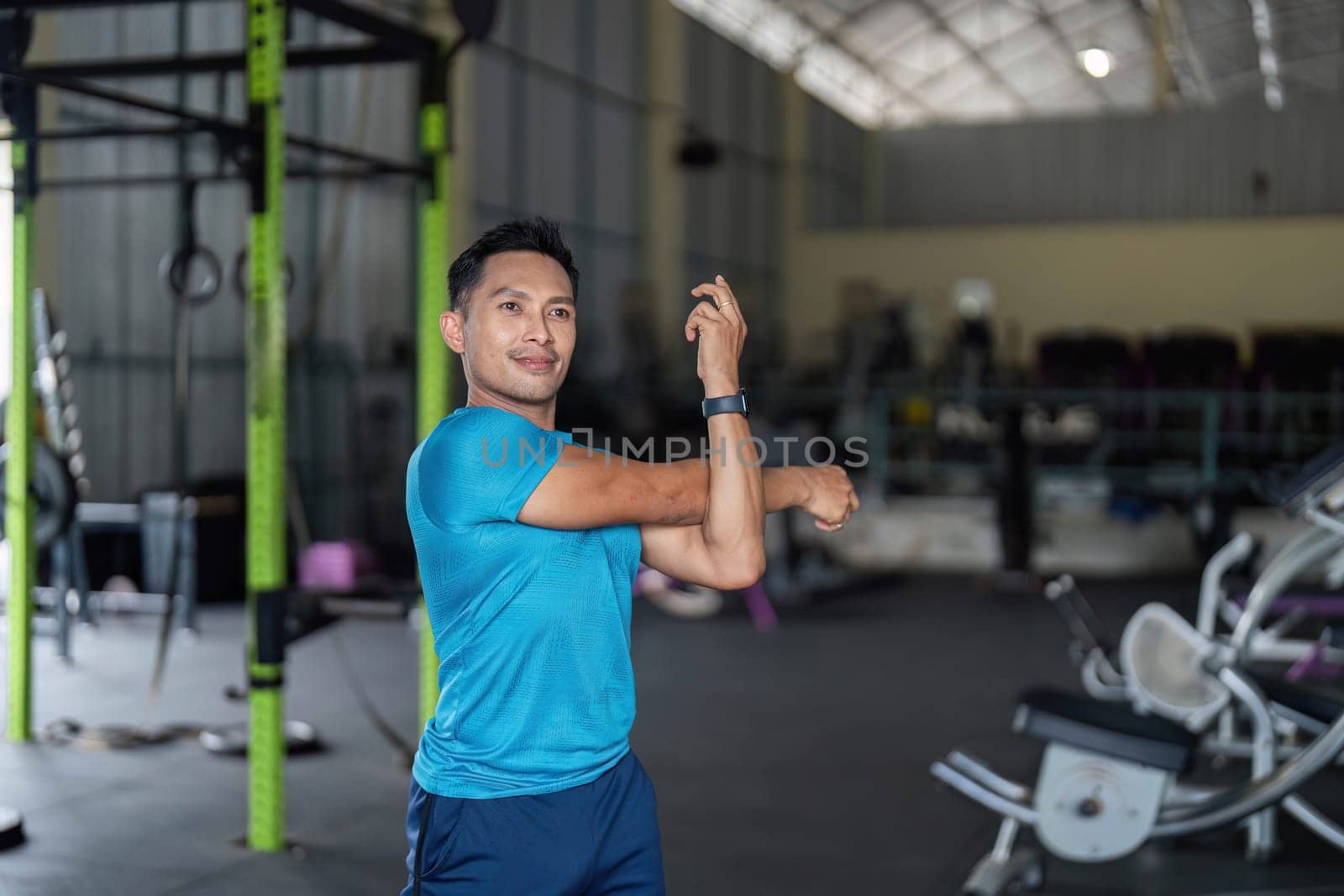 A fit man stretches his arms in a gym, focusing on flexibility and preparing for an intense workout session.