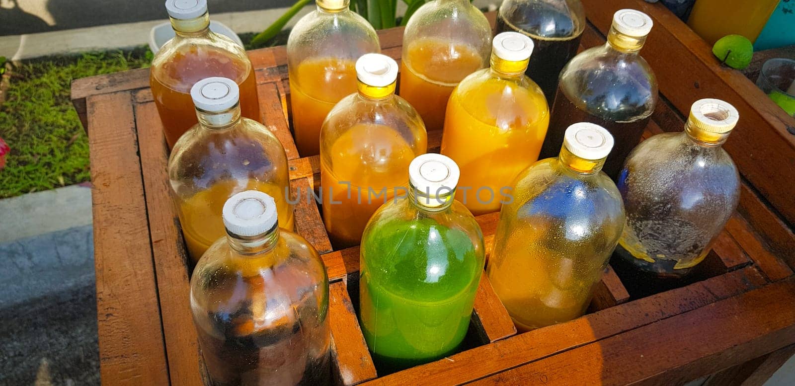 Colorful Bottles of traditional natural organic medicine locally called jamu, Displayed in Wooden Case on a Sunny Day, Various colorful bottles filled with liquids arranged in a wooden container outdoors under sunlight.