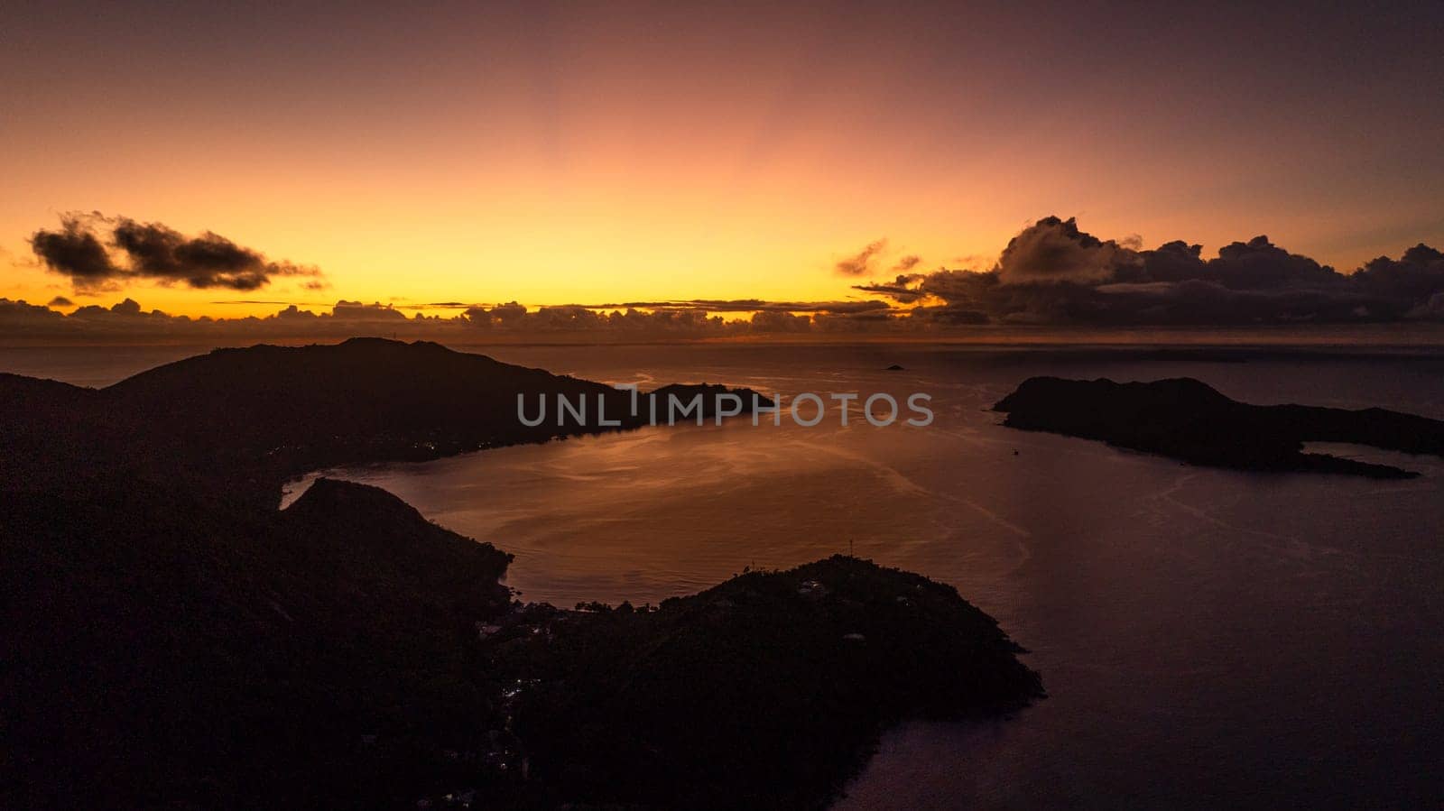 A fiery sunset bathes the horizon in warm light, while the islands and water rest in shadows. Praslin, Seychelles.