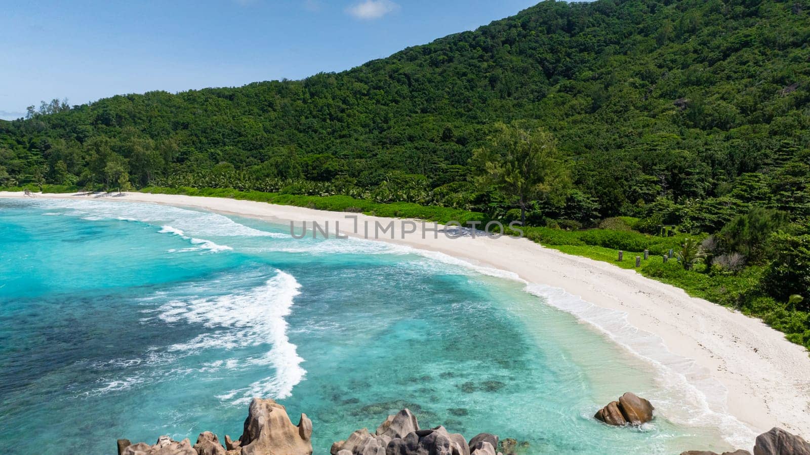 A pristine tropical beach with turquoise waves and white sand, surrounded by lush greenery. Anse Cocos. Seychelles, La Digue.