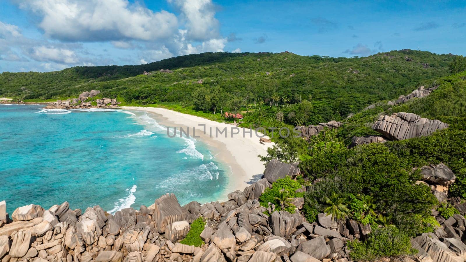 A turquoise beach surrounded by lush greenery and large rocky formations. Grand Anse Beach, La Digue, Seychelles.