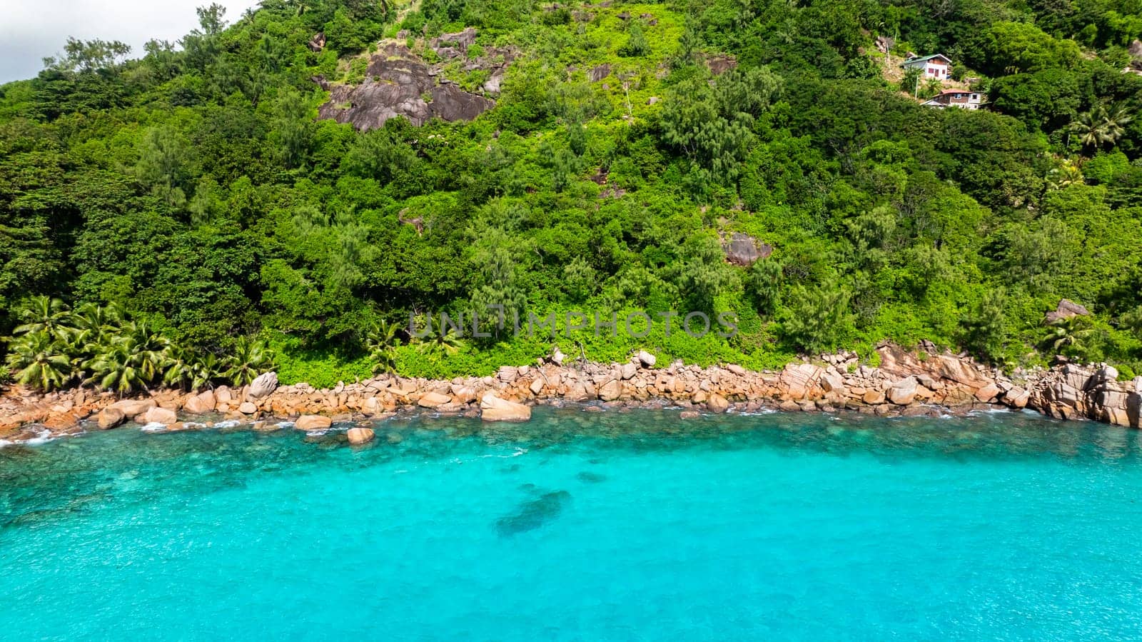 The vibrant meeting of turquoise waters and rugged rocky shores flanked by dense greenery. Praslin, Seychelles.