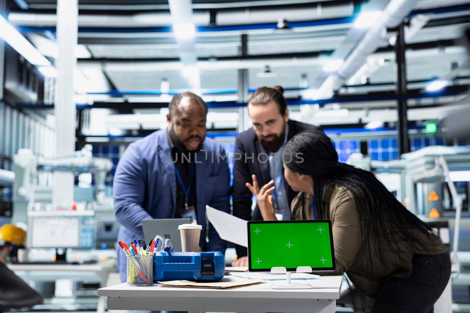 Multiethnic energy specialists coordinates activity next to chroma key, taking quality control measures in a solar tech facility. Corporate oversight and industrial execution.