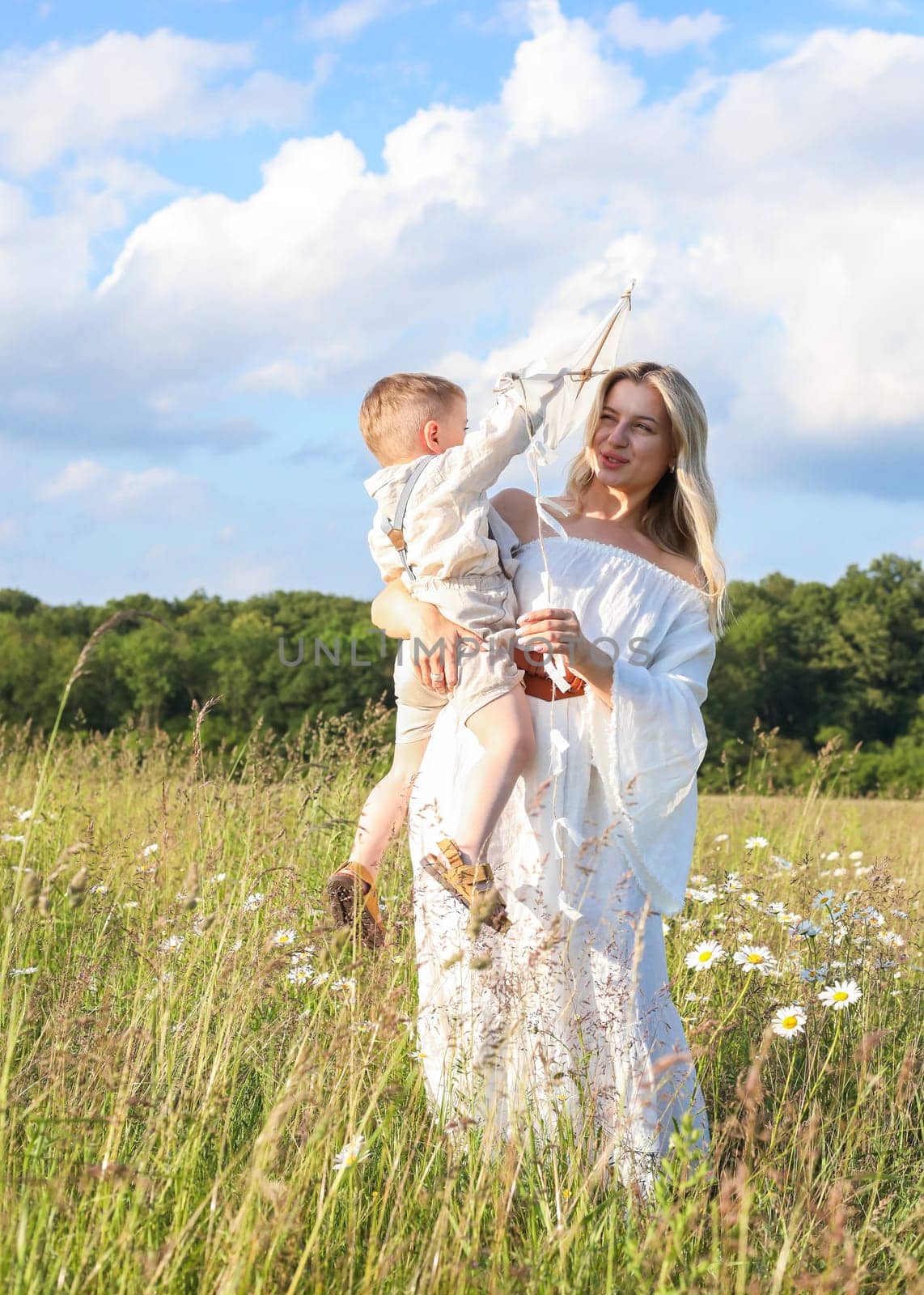 A small child in his mother's arms, they are having fun in the meadow, flying a kite. High quality photo