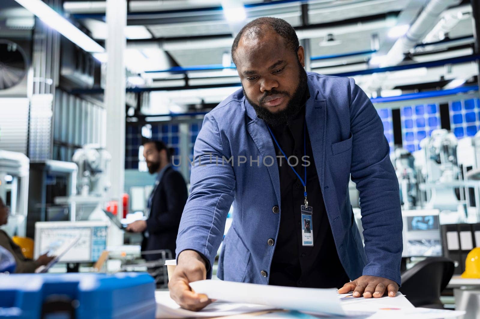 Black male sustainability consultant in suit evaluates solar panel systems and the production line in a modern factory, guiding operations toward clean energy and industrial efficiency.