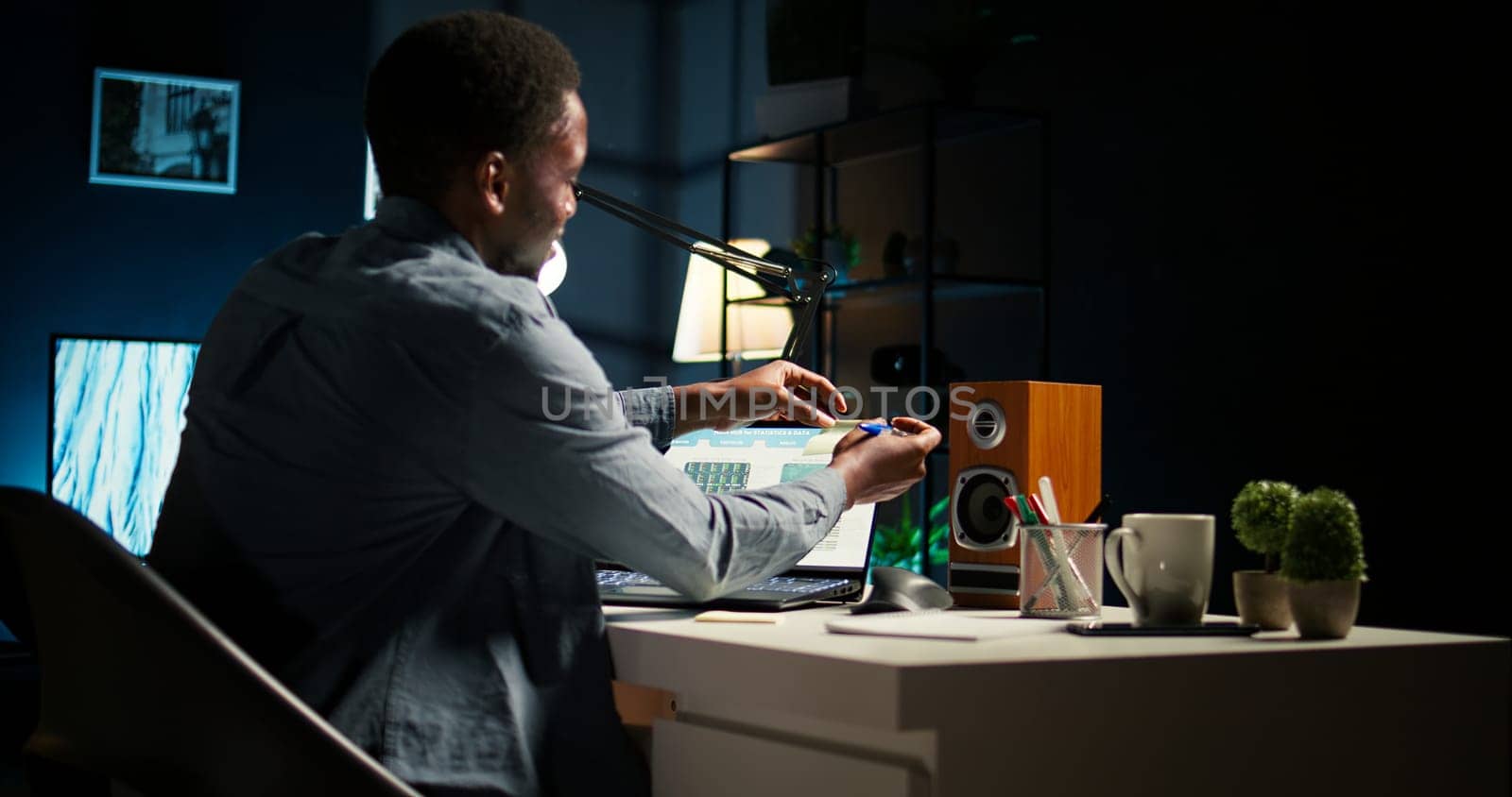 Black man organizing his schedule with a planner and putting a reminder, creating an adhesive note post it and browsing the web. Modern productive guy writes a memo for research. Camera A.