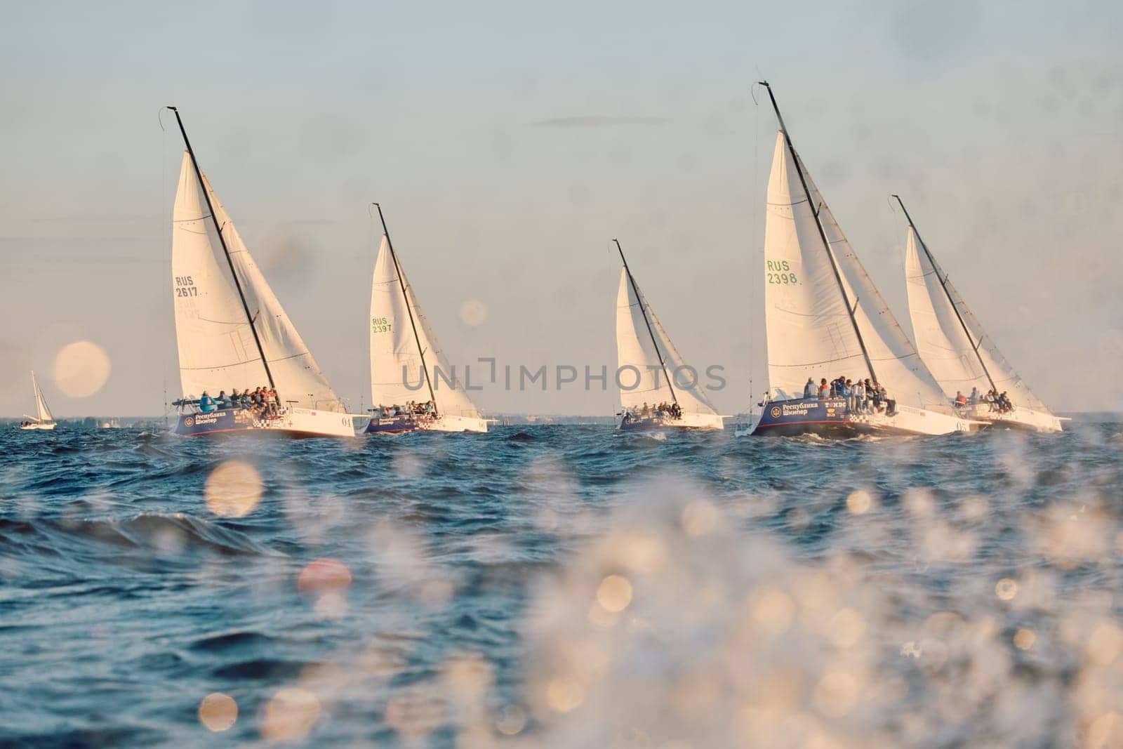 Russia, St.Petersburg, 07 June 2024: Sailing regatta in the Gulf of Finland at sunset, hot race of several yachts, teamwork, yachtsmen sitting on board the boat. High quality photo