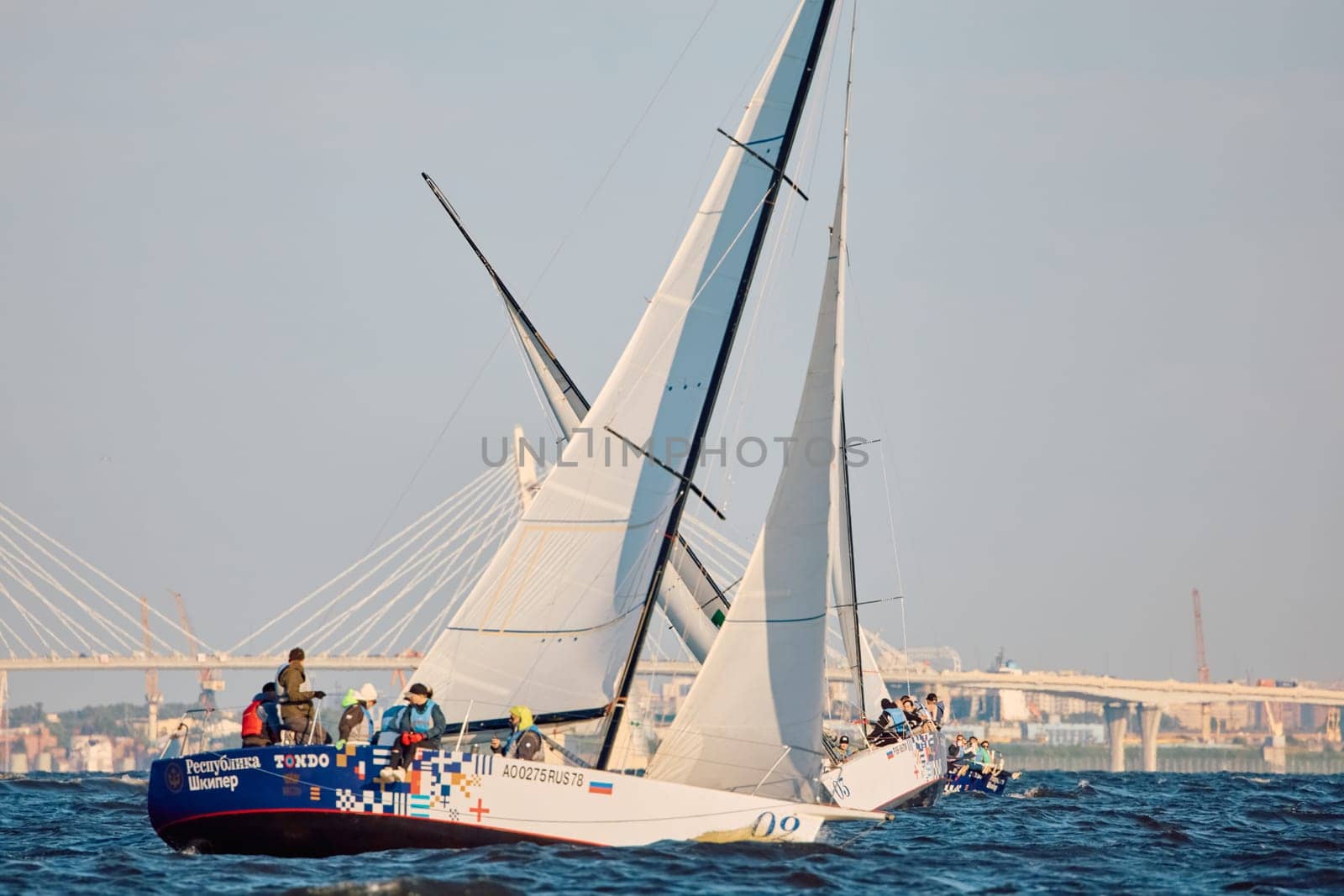 Russia, St.Petersburg, 07 June 2024: Sailing regatta in the Gulf of Finland at sunset, hot race of several yachts, teamwork, yachtsmen sitting on board the boat. High quality photo
