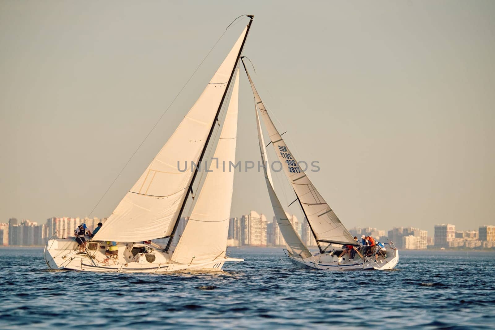 Russia, St.Petersburg, 24 May 2024: Sailing regatta in the Gulf of Finland at sunset, hot race of several yachts, teamwork, yachtsmen sitting on board the boat. High quality photo