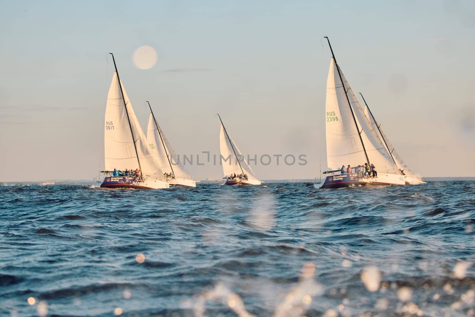 Russia, St.Petersburg, 07 June 2024: Sailing regatta in the Gulf of Finland at sunset, hot race of several yachts, teamwork, yachtsmen sitting on board the boat. High quality photo