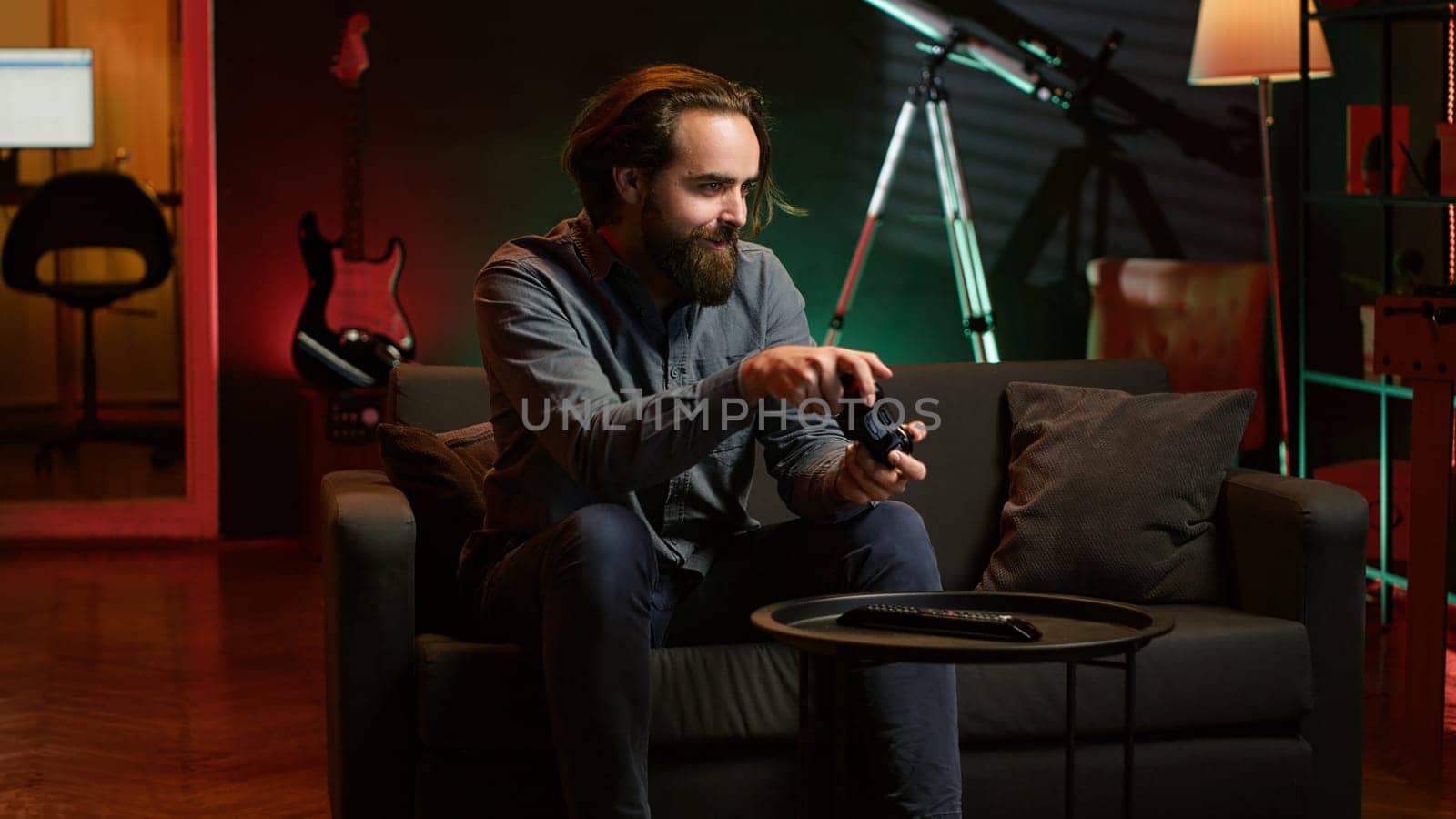 Cheerful gamer rushing home to play newly released game. Happy man jumping on couch, eager to play videogame on console, relaxing after hard day at work, camera A slow motion shot