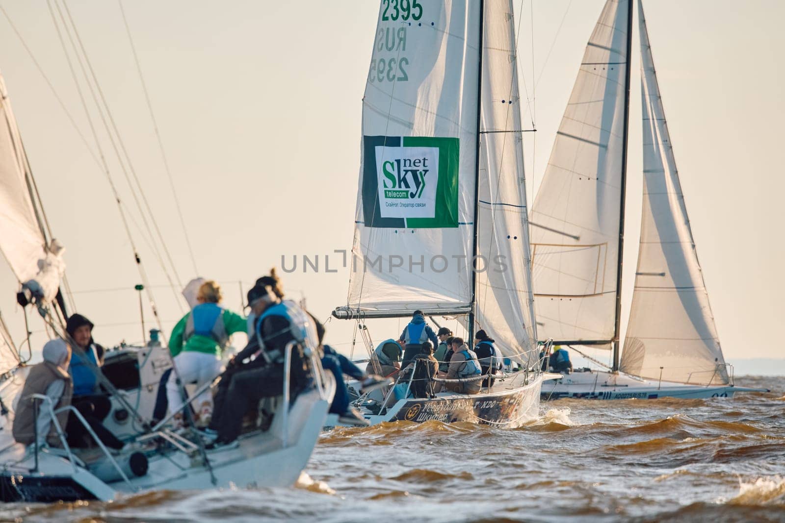 Russia, St.Petersburg, 07 June 2024: Sailing regatta in the Gulf of Finland at sunset, hot race of several yachts, teamwork, yachtsmen sitting on board the boat. High quality photo