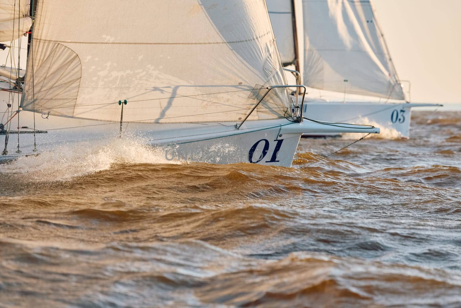 Sailing regatta in the Gulf of Finland at sunset, the bows of two sailing yachts competing in a race, splashing water from under the boats, teamwork, board the boat. High quality photo