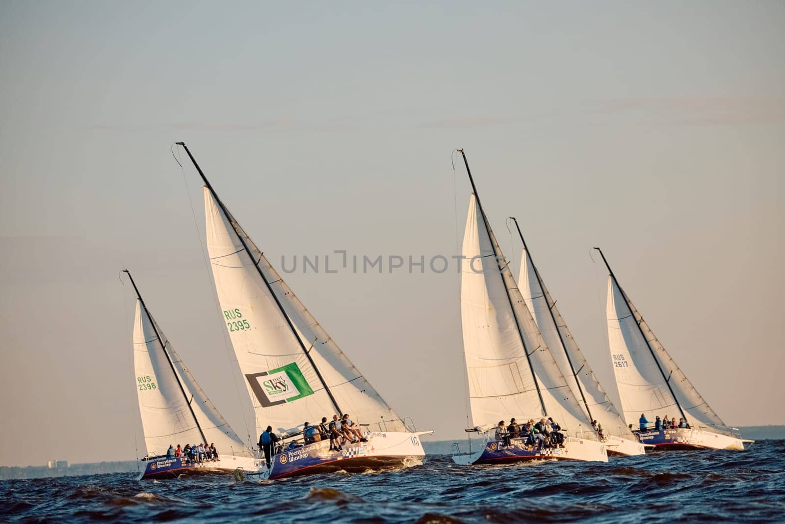 Russia, St.Petersburg, 07 June 2024: Sailing regatta in the Gulf of Finland at sunset, hot race of several yachts, teamwork, yachtsmen sitting on board the boat. High quality photo