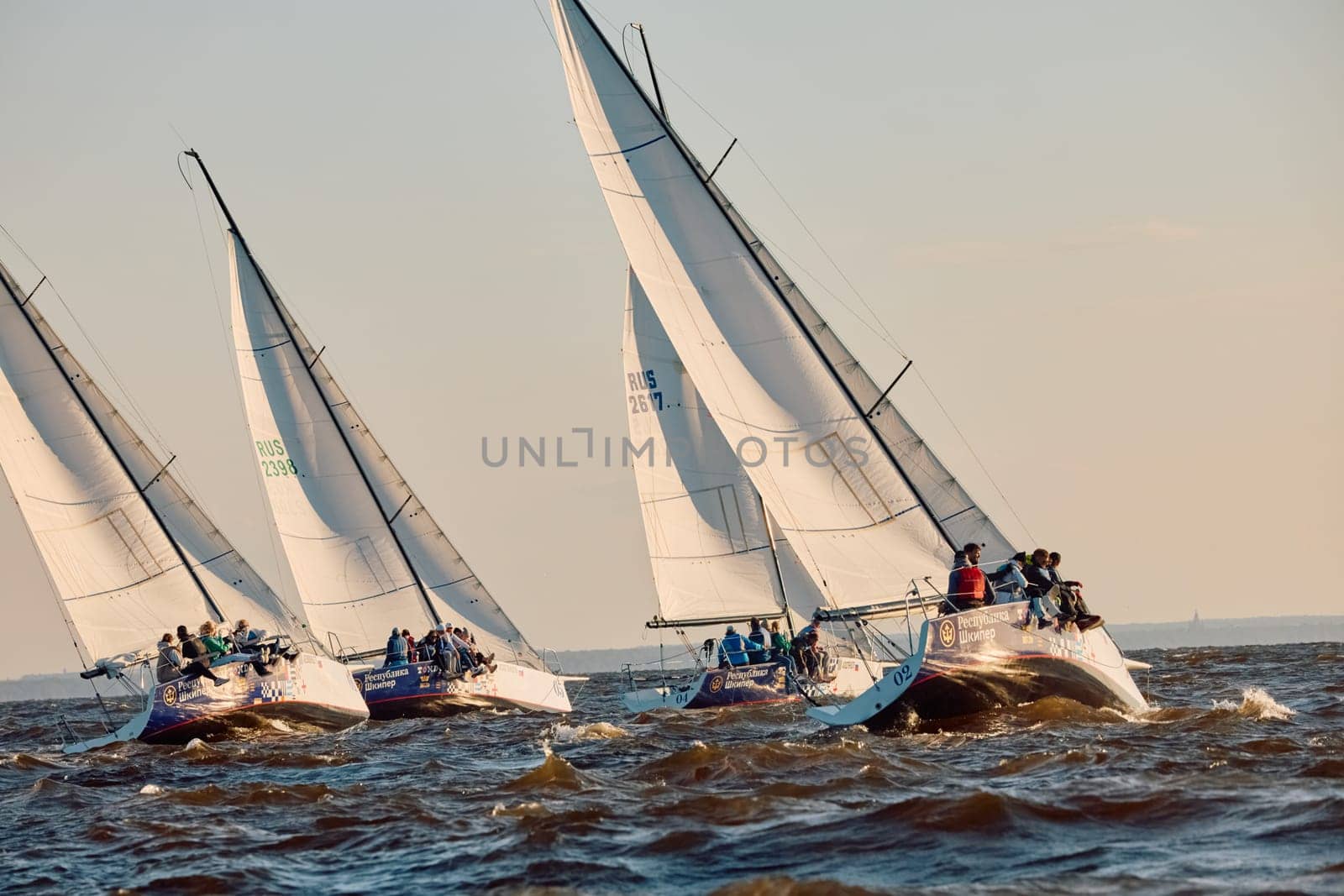 Russia, St.Petersburg, 07 June 2024: Sailing regatta in the Gulf of Finland at sunset, hot race of several yachts, teamwork, yachtsmen sitting on board the boat. High quality photo
