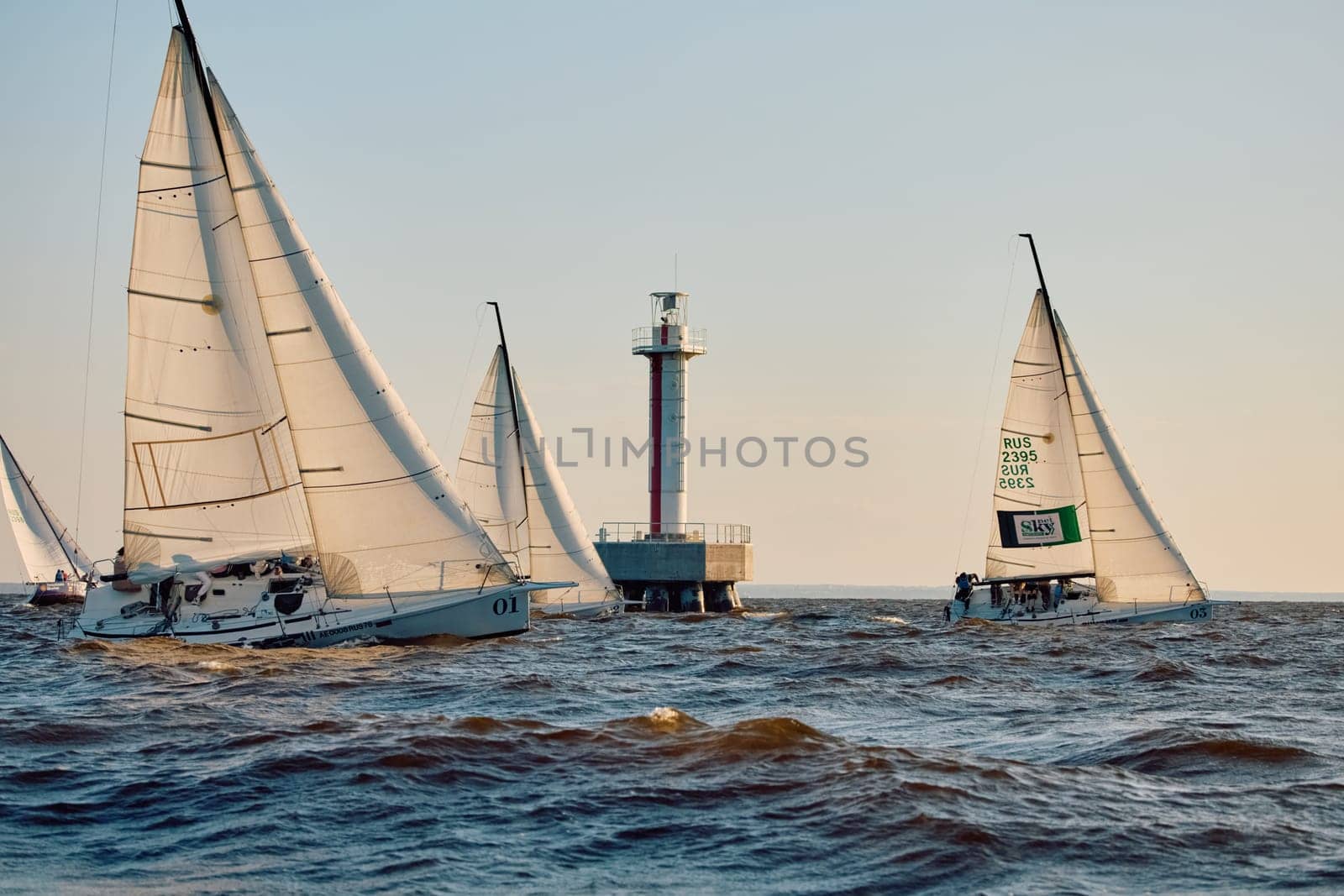 Russia, St.Petersburg, 07 June 2024: Sailing regatta in the Gulf of Finland at sunset, hot race of several yachts, teamwork, yachtsmen sitting on board the boat. High quality photo