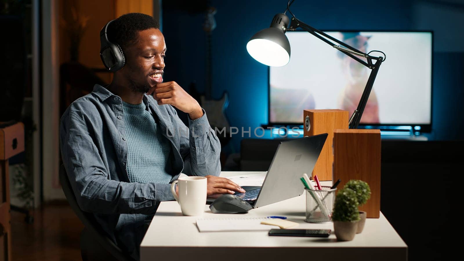 Young focused freelancer attending an online meeting from his home office, discussing with associates remotely. Smiling black man engages in virtual communication, remote technology. Camera B.