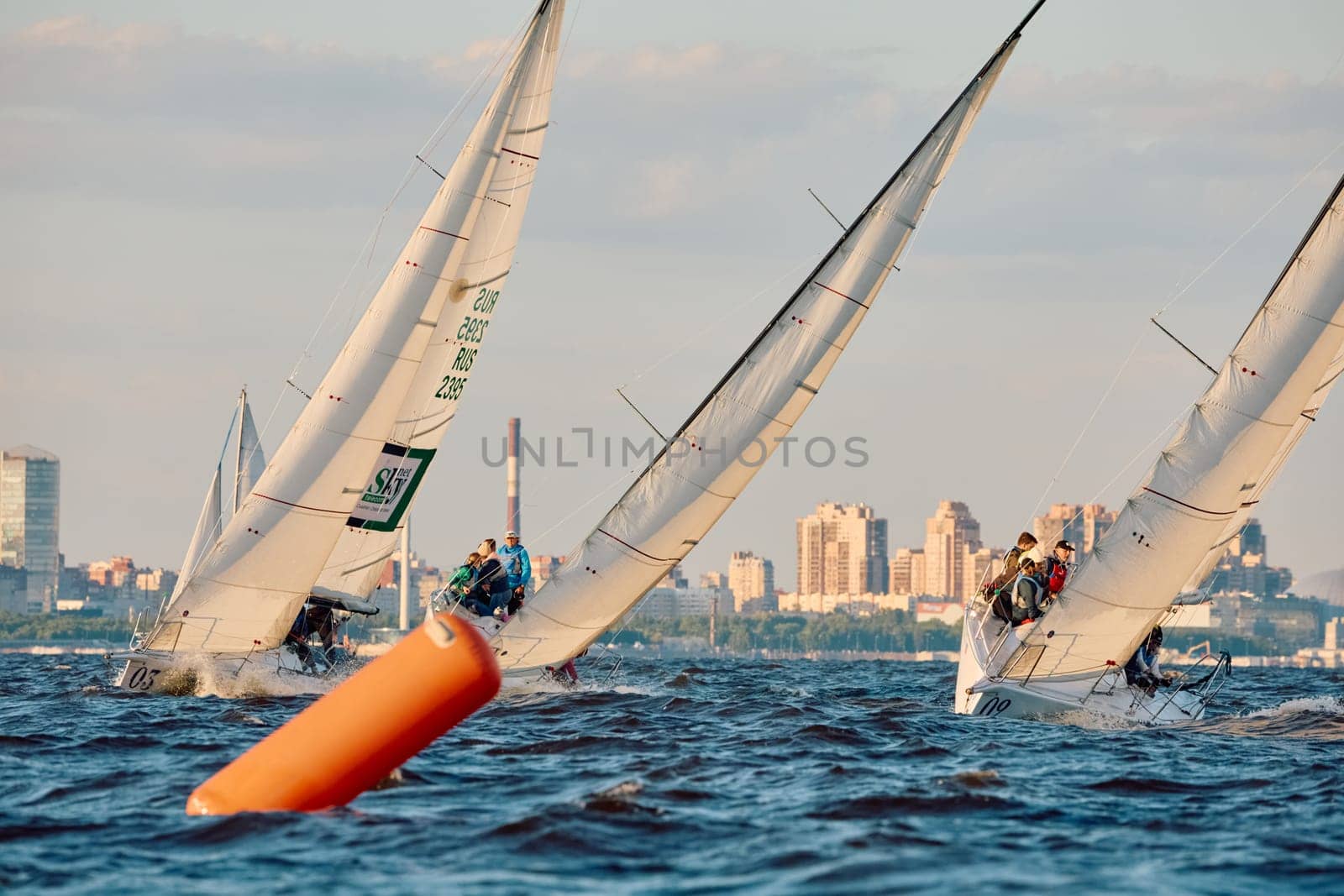 Russia, St.Petersburg, 07 June 2024: Sailing regatta in the Gulf of Finland at sunset, hot race of several yachts, teamwork, yachtsmen sitting on board the boat. High quality photo