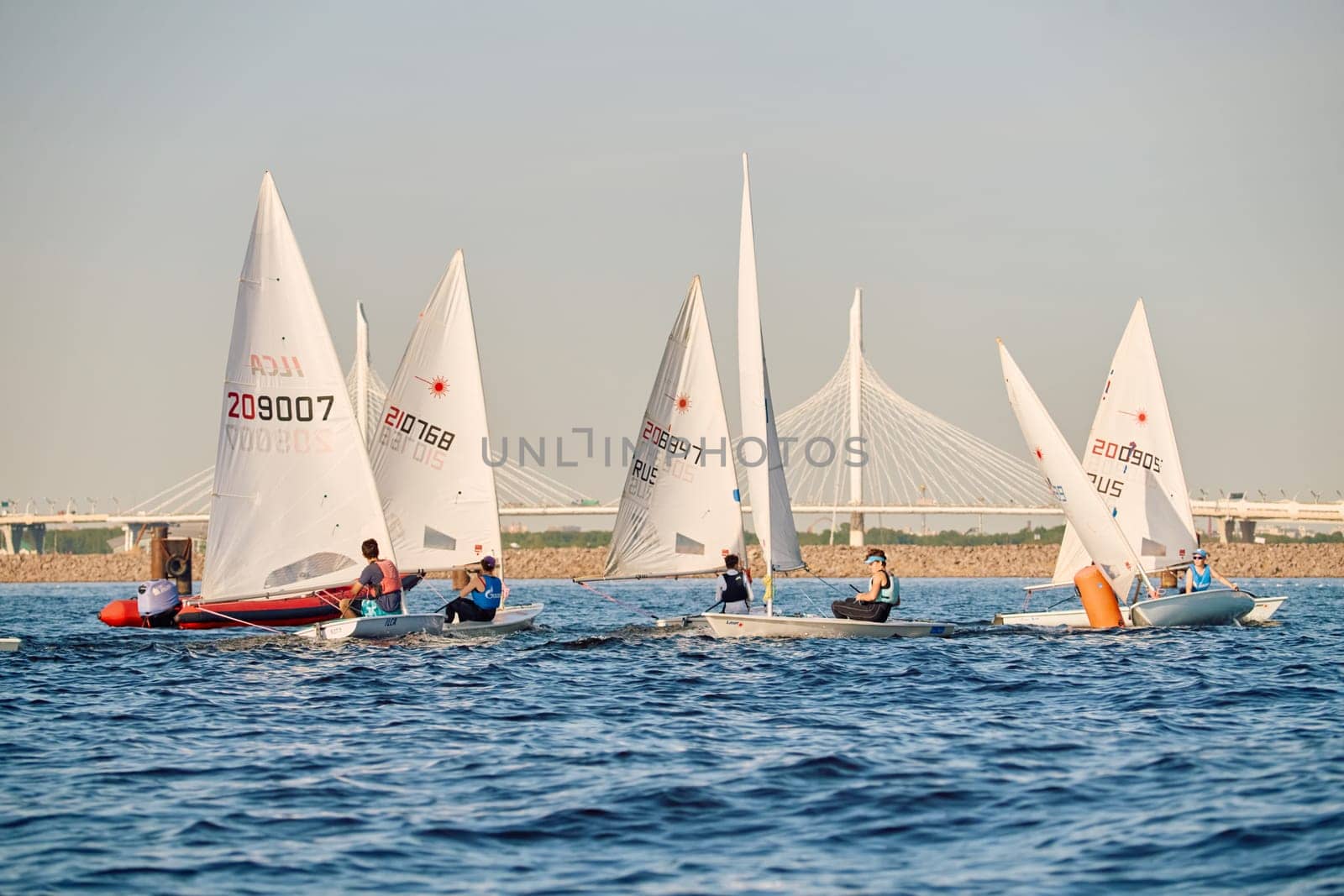 Russia, St.Petersburg, 24 May 2024: Sailing regatta in the Gulf of Finland at sunset, hot race of several yachts, teamwork, yachtsmen sitting on board the boat. High quality photo
